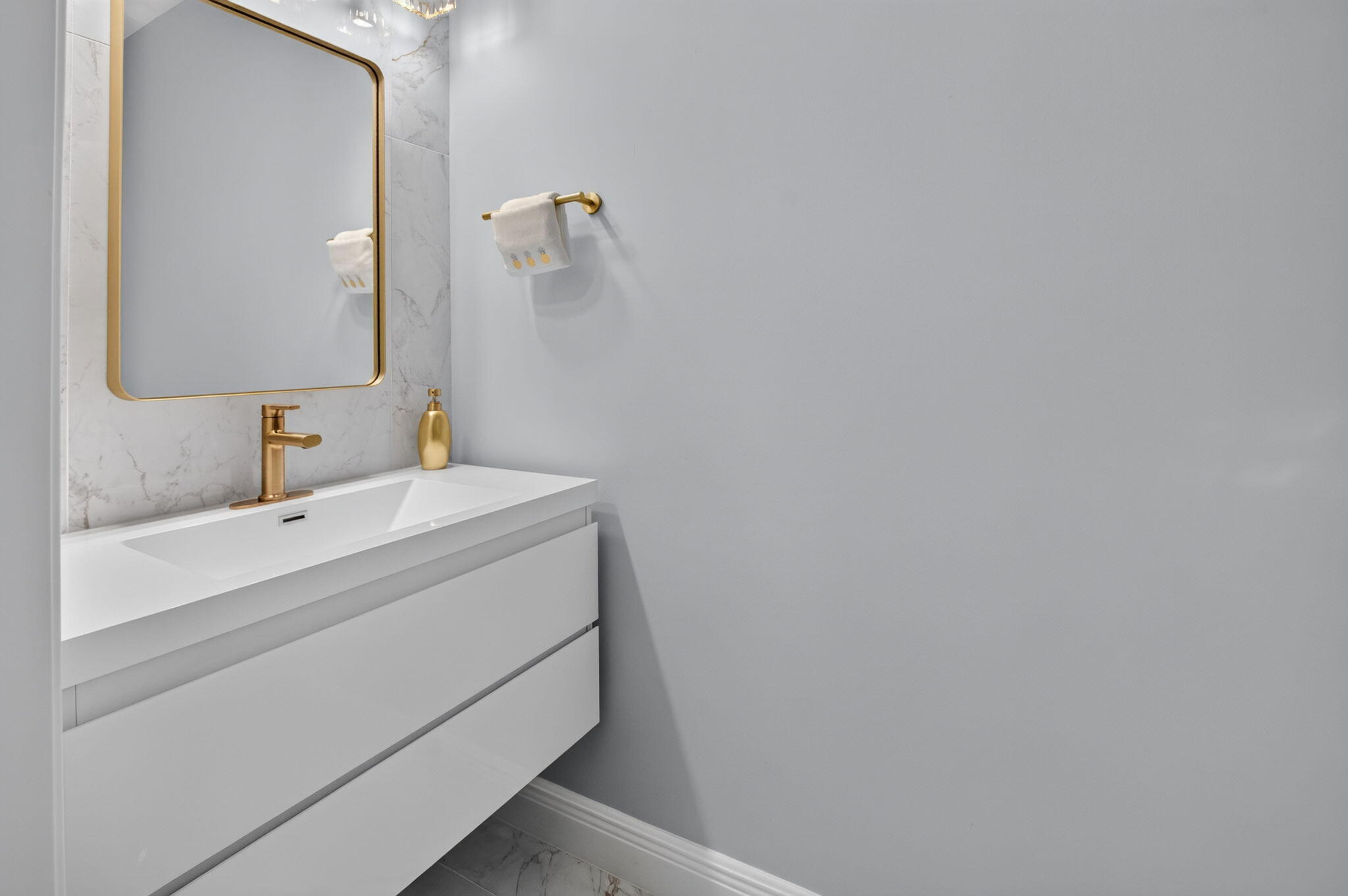 Modern bathroom vanity with a white sink, gold fixtures, and marble backsplash.