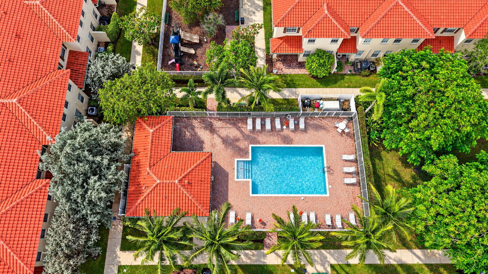 Aerial view of a community pool with a brick deck, lounge chairs, and palm trees.