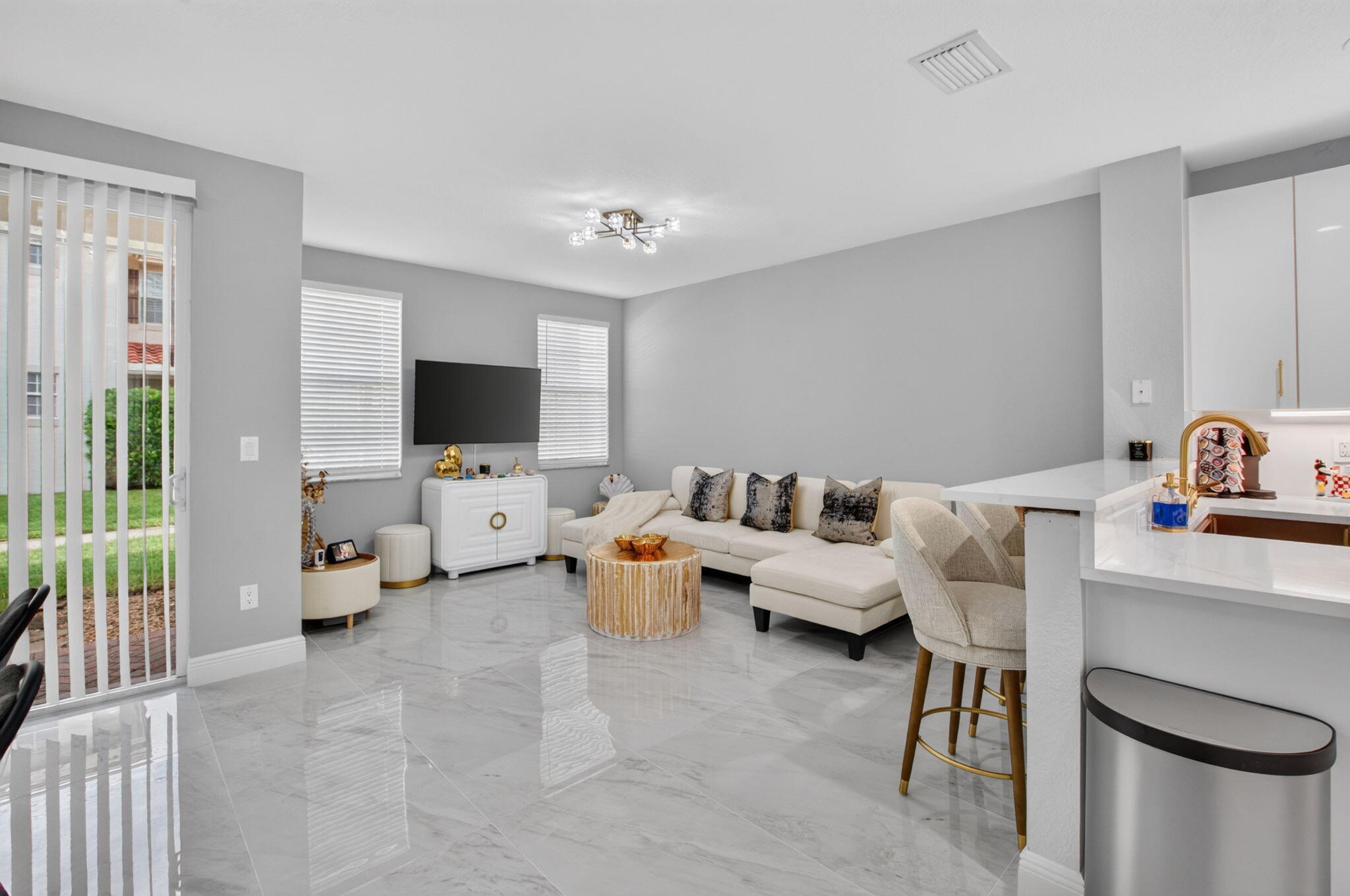 Open-plan living room with a white sectional, marble-look floors, breakfast bar, and sliding glass door.