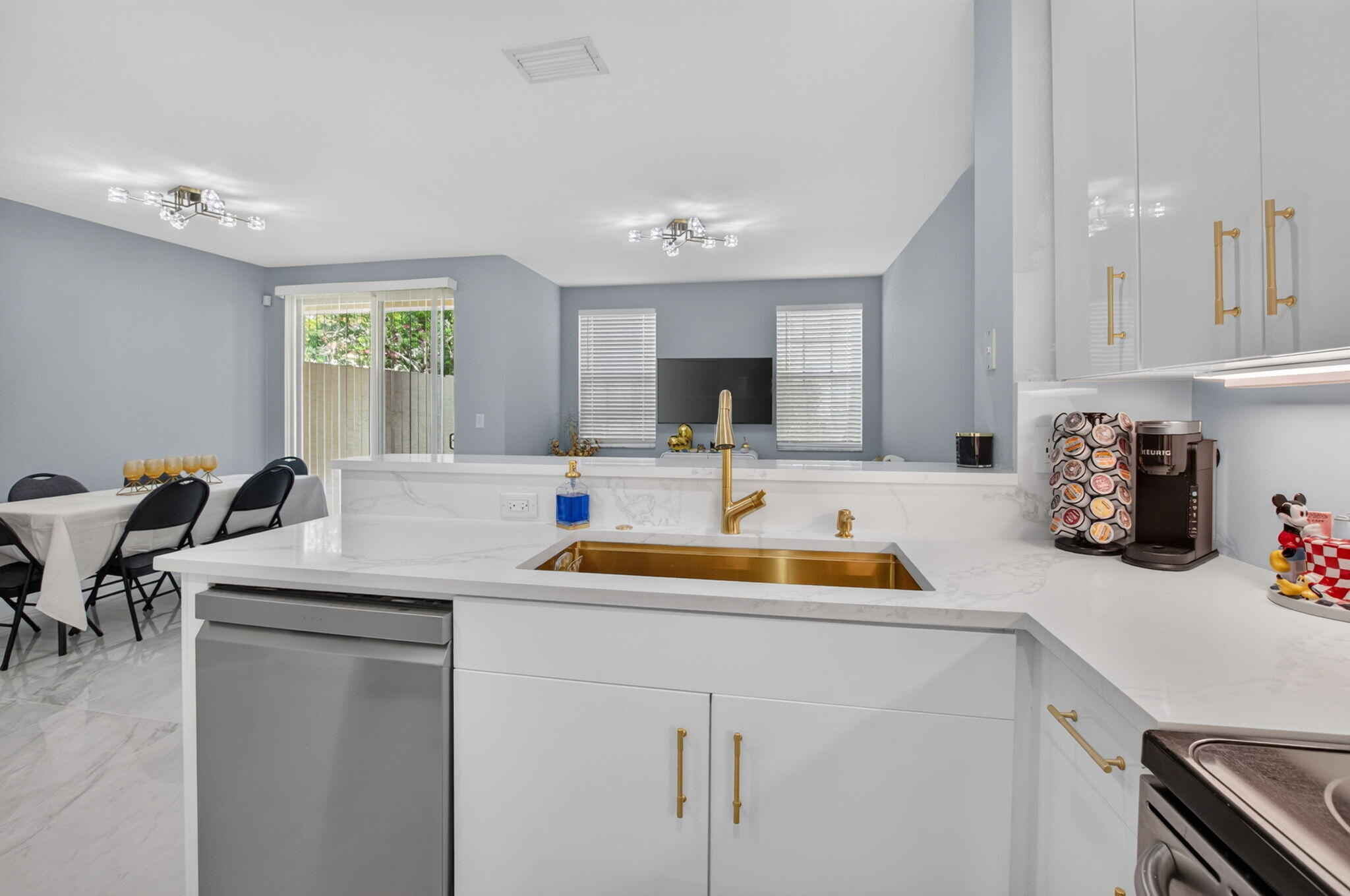 Renovated kitchen with a marble-look island, gold sink and faucet, and dining area beyond.