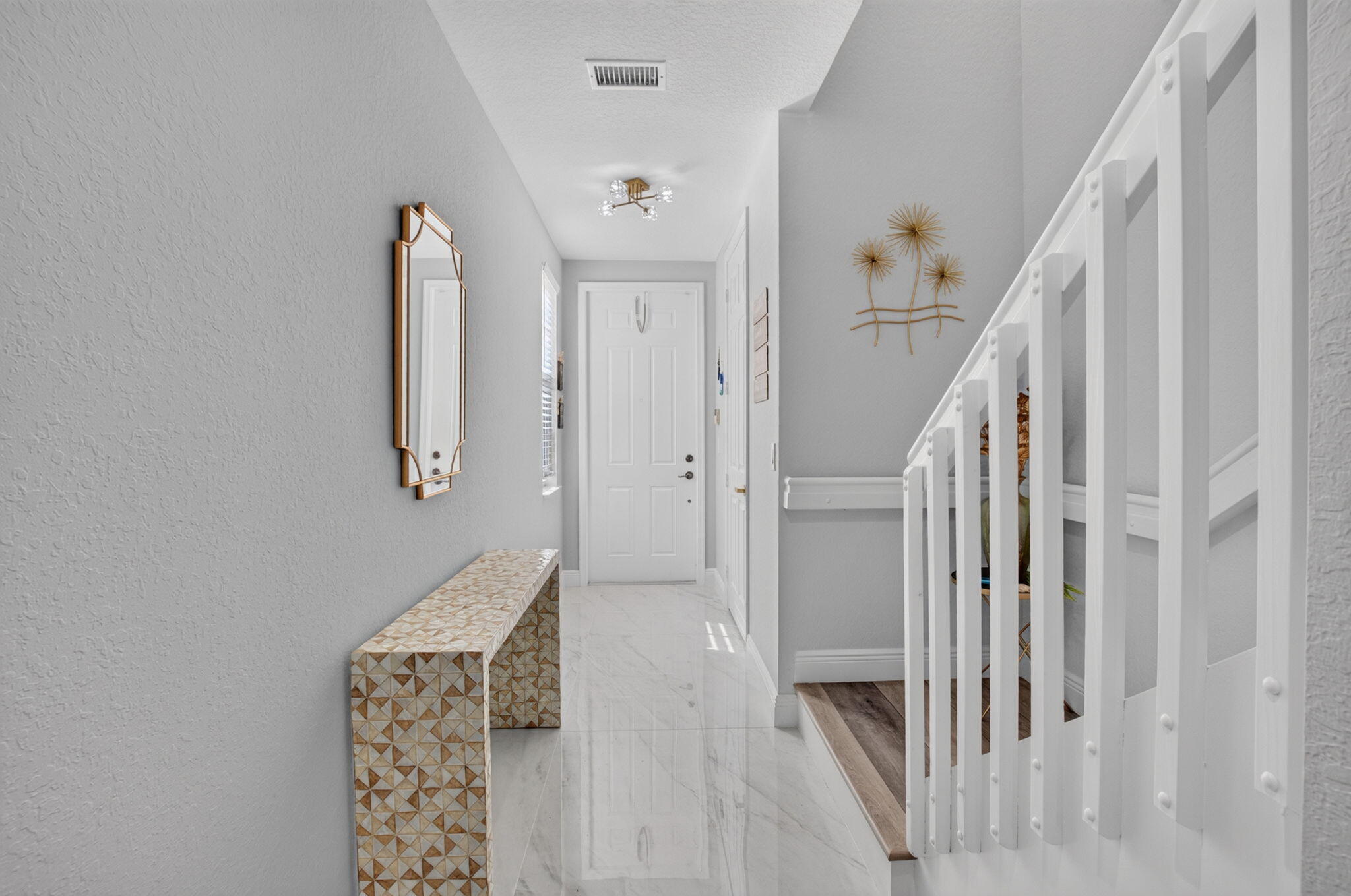Furnished entry hallway with a patterned bench, glossy tile floor, and white staircase railing.