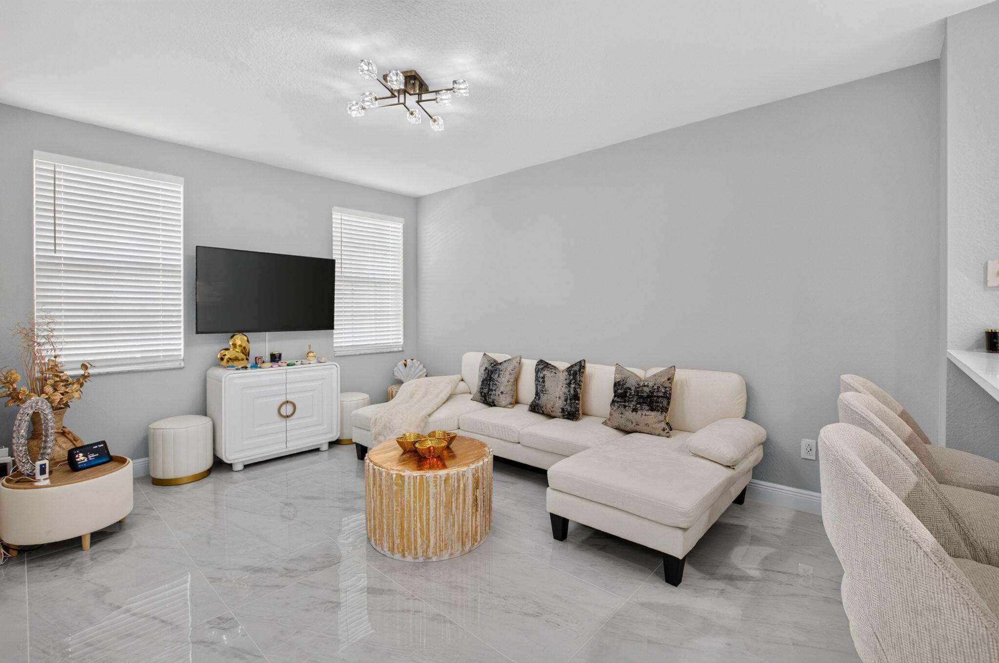 Living room with a white sectional, glossy tile floors, and a round gold-toned coffee table.