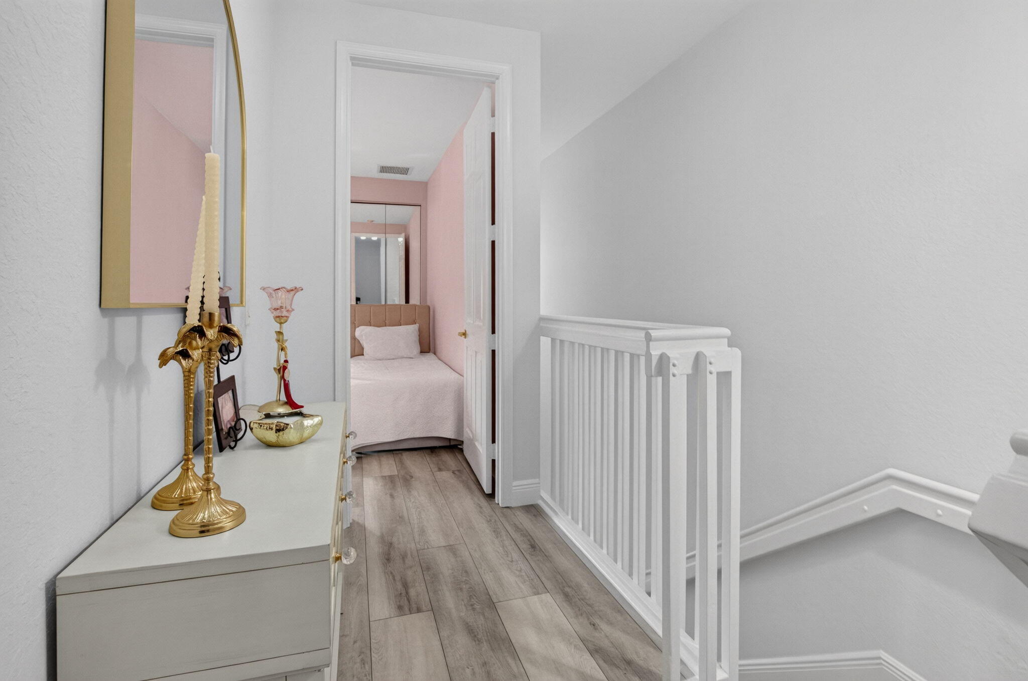 Upstairs hallway with white stair railing, gray flooring, and a view into a pink bedroom.