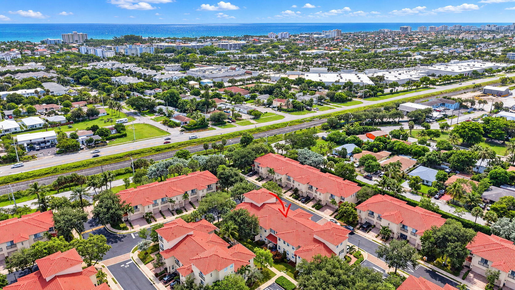 Aerial view of a red-roofed condominium marked by an arrow, with the coastline in the distance.