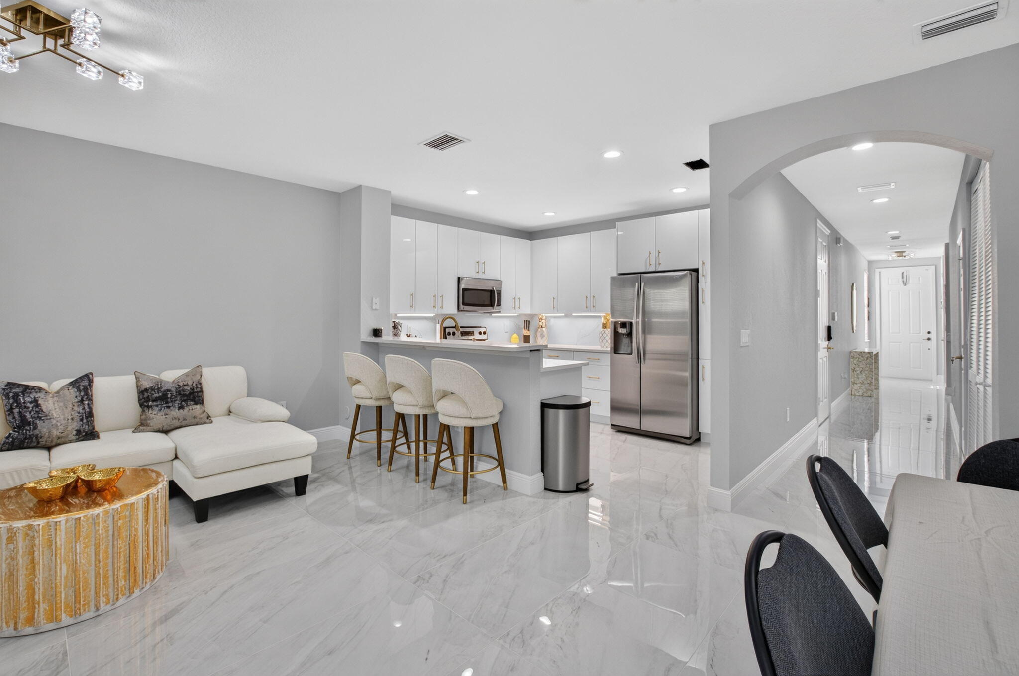 Open-plan kitchen with white cabinets, stainless steel appliances, and a breakfast bar beside a furnished living area.