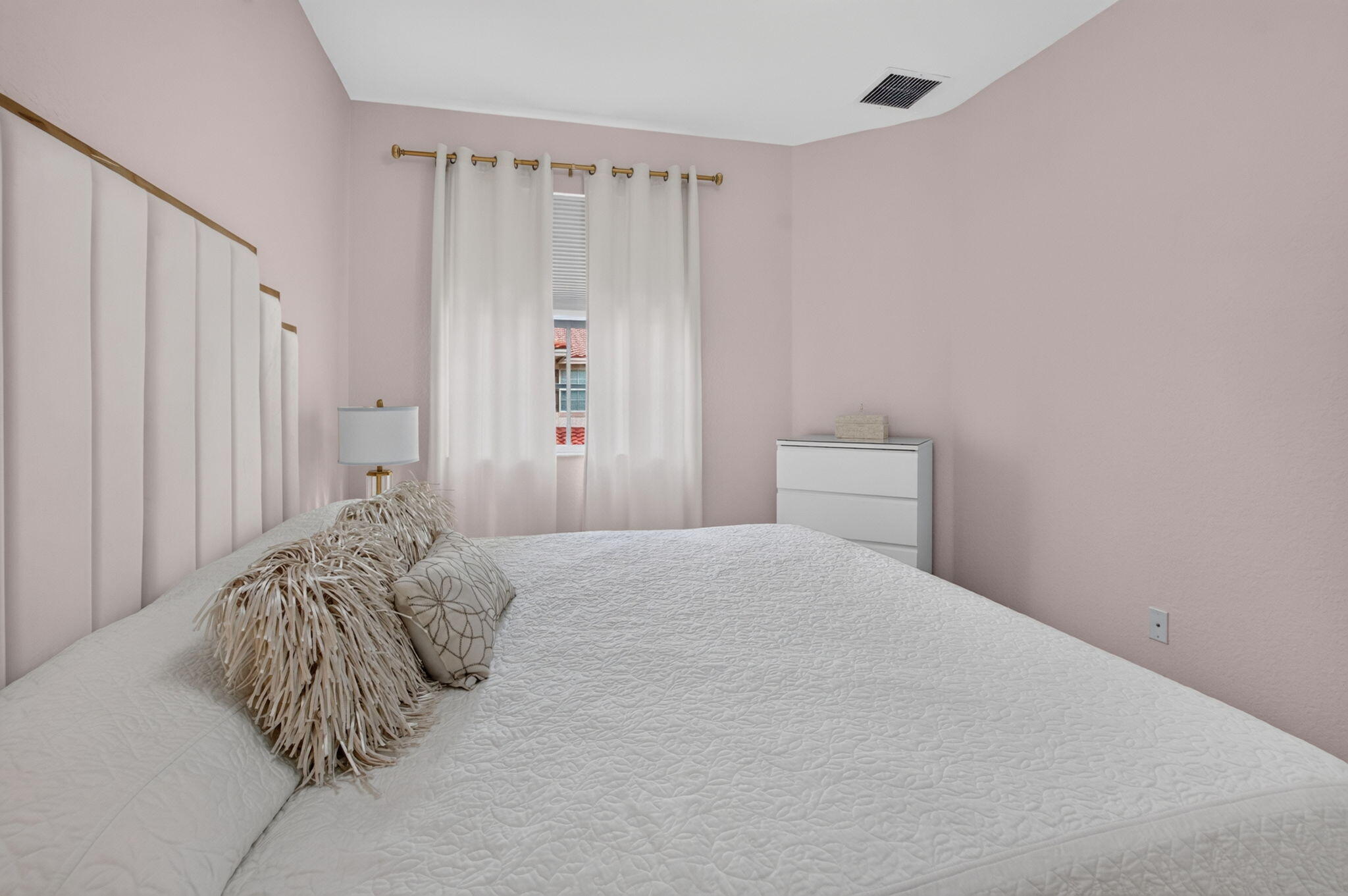 Bedroom with a white quilted bed, pale pink walls, and a padded headboard.