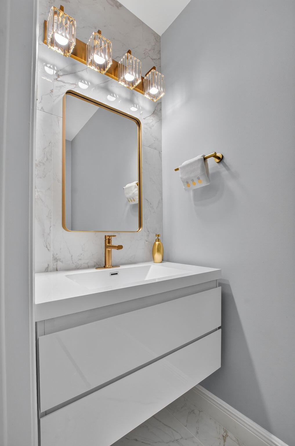 Modern bathroom vanity with a gold-framed mirror, marble-look tile, and gold fixtures.