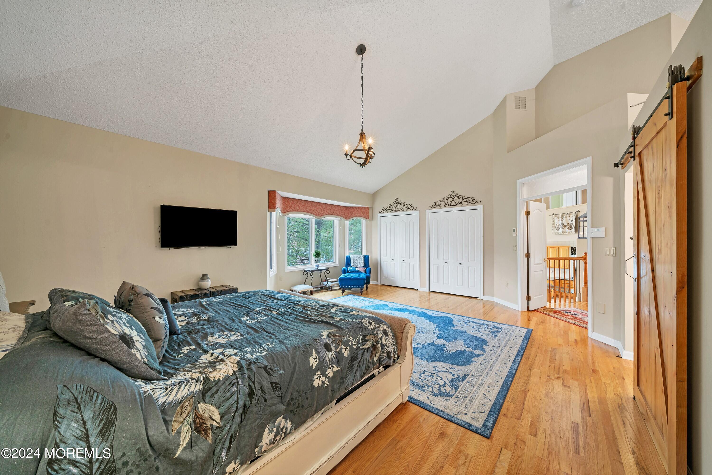 Furnished bedroom with vaulted ceiling, hardwood floors, bay windows, and a wooden sliding barn door.