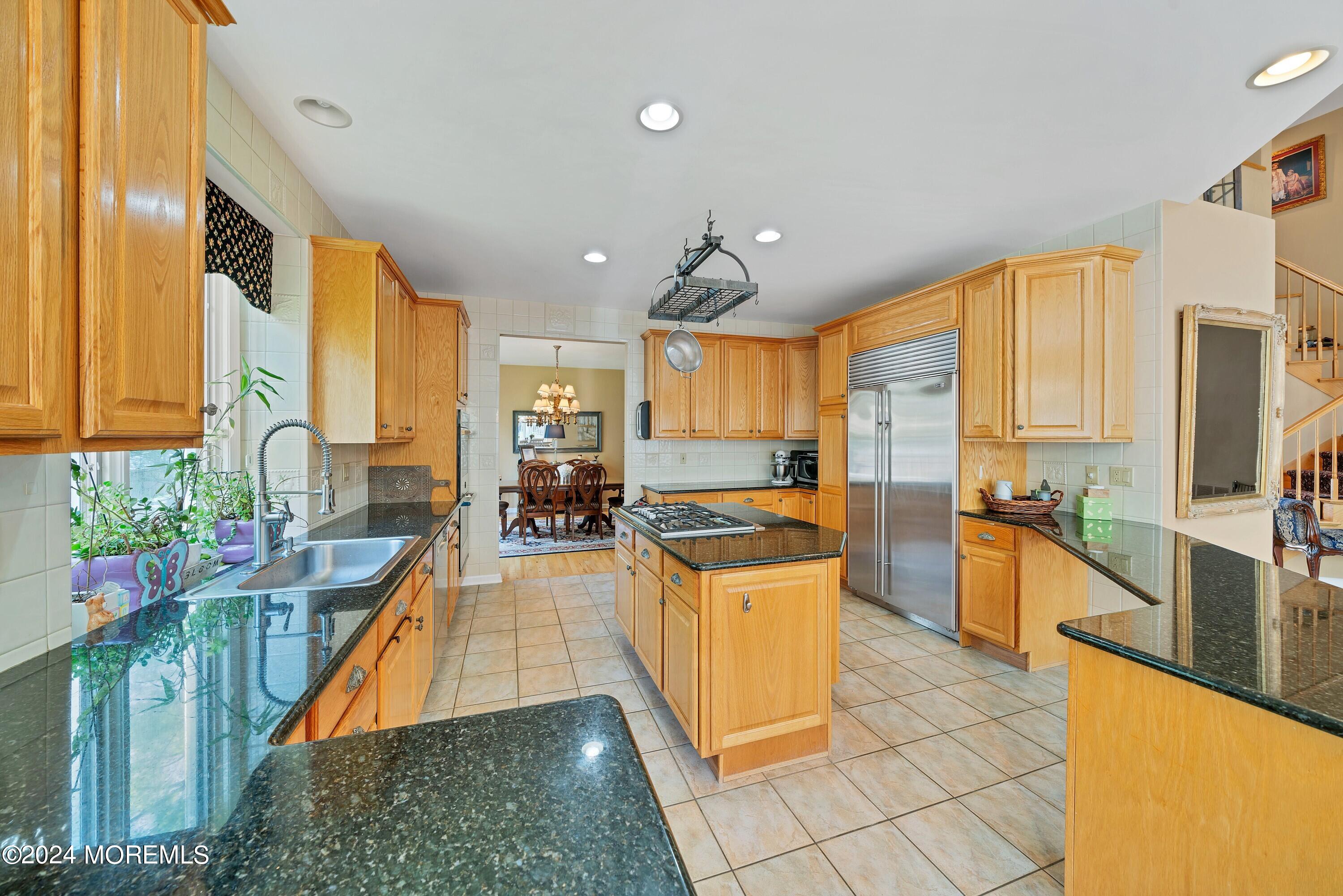 Kitchen with honey-colored cabinets, granite counters, a cooktop island, and stainless-steel refrigerator.