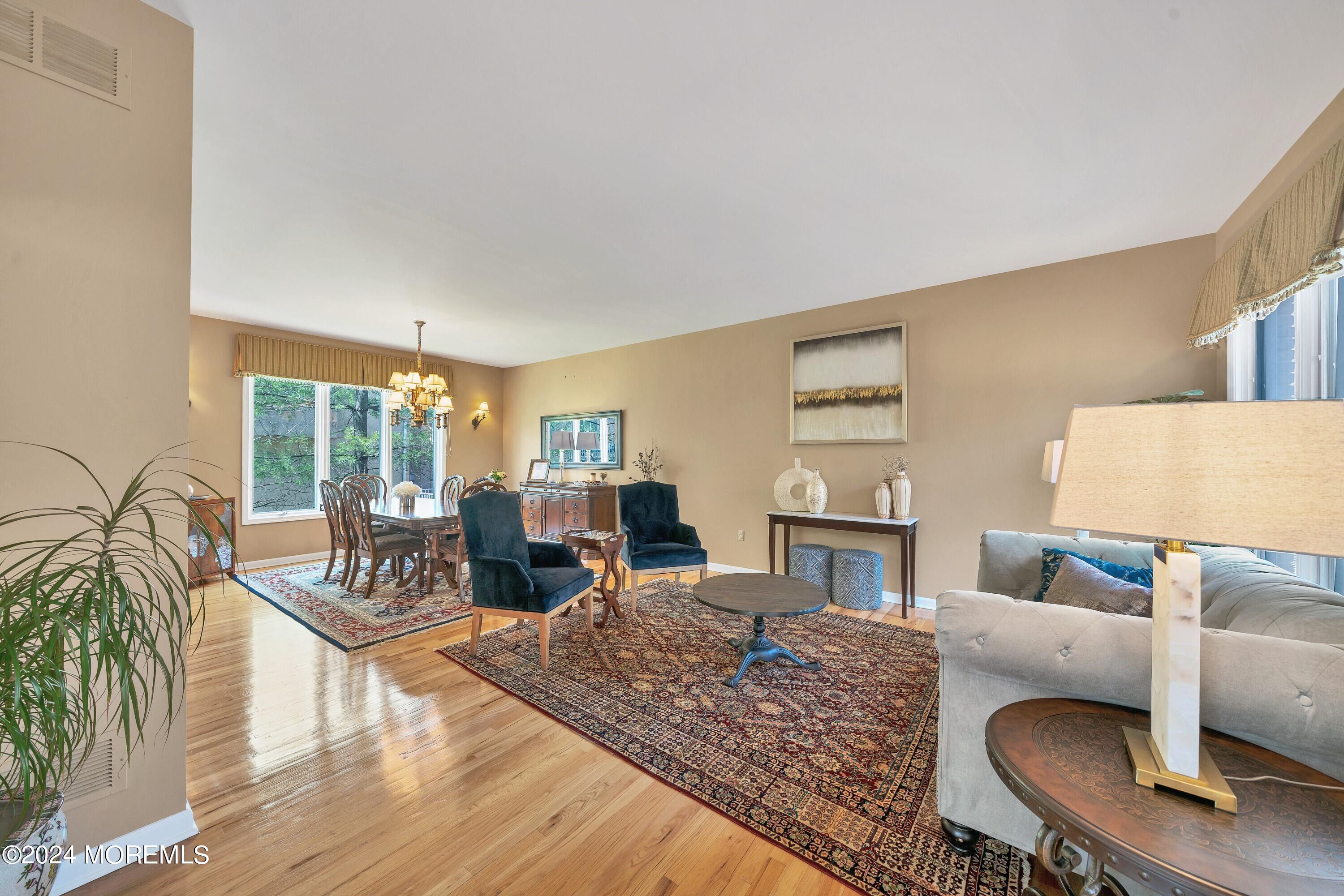 Open-plan living and dining room with hardwood floors, patterned rugs, and a chandelier over the dining table.