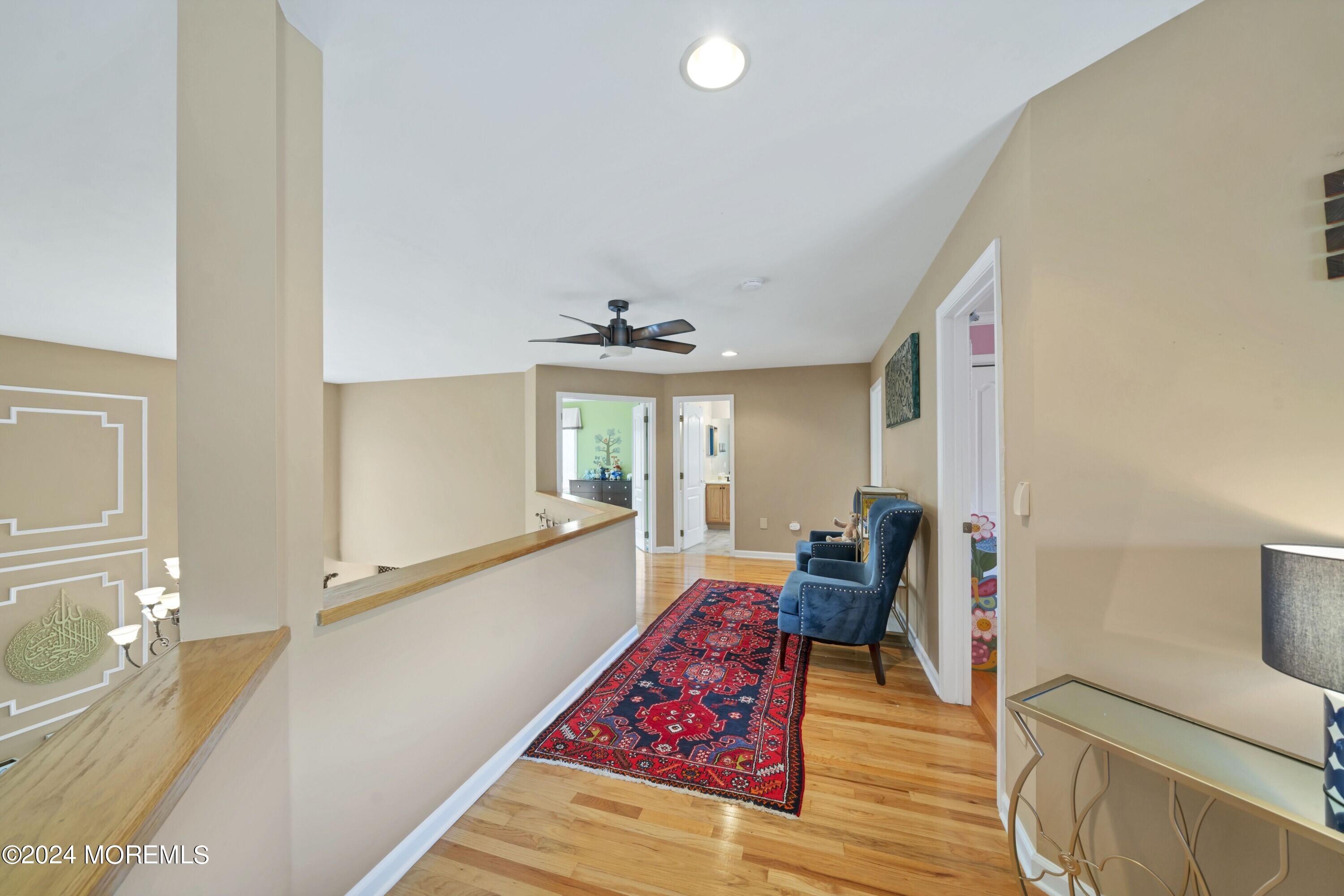 Upstairs hallway with a red patterned runner, blue chairs, hardwood floors, and an open stair railing.