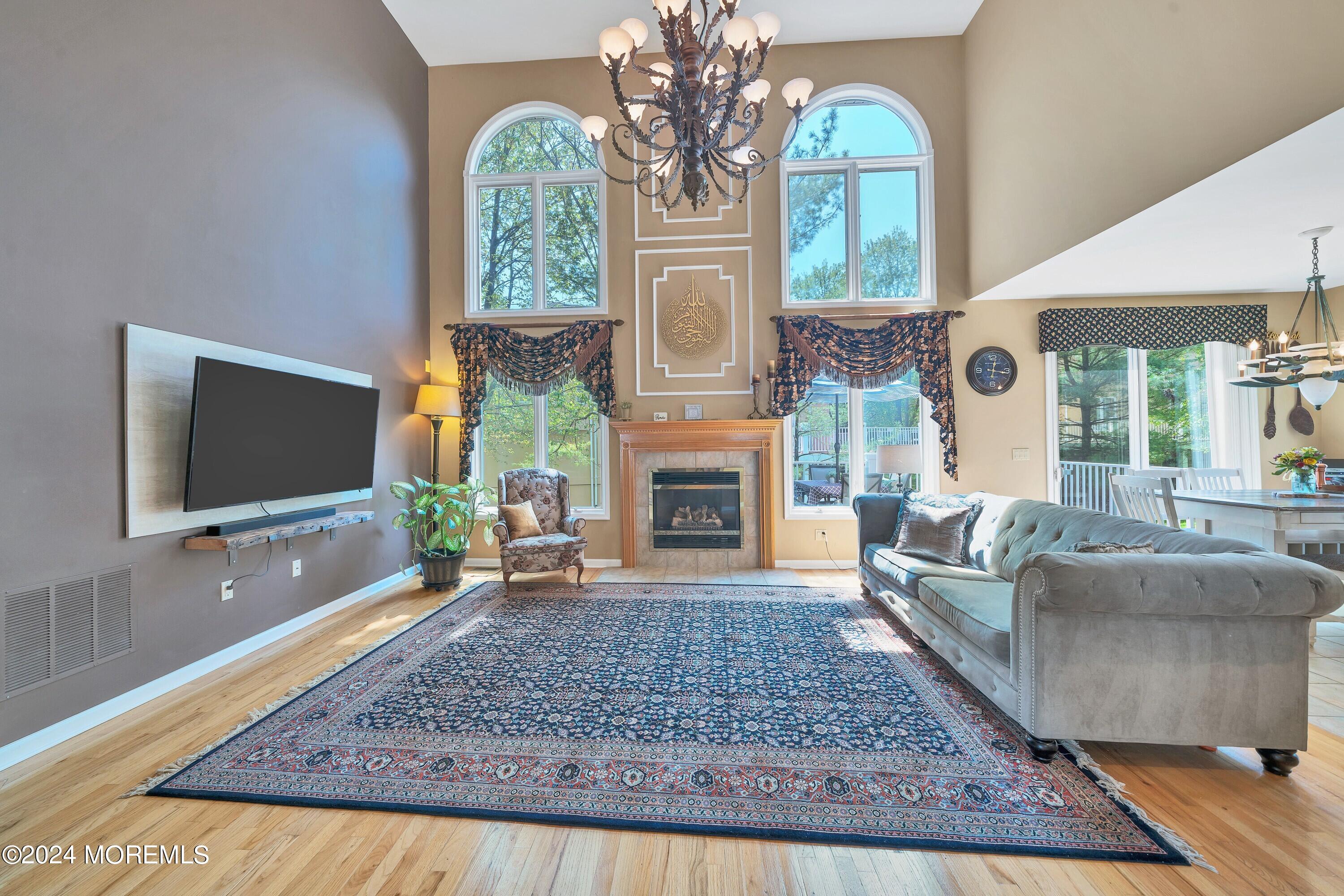 Furnished living room with vaulted ceiling, arched windows, fireplace, gray sectional, and patterned rug.