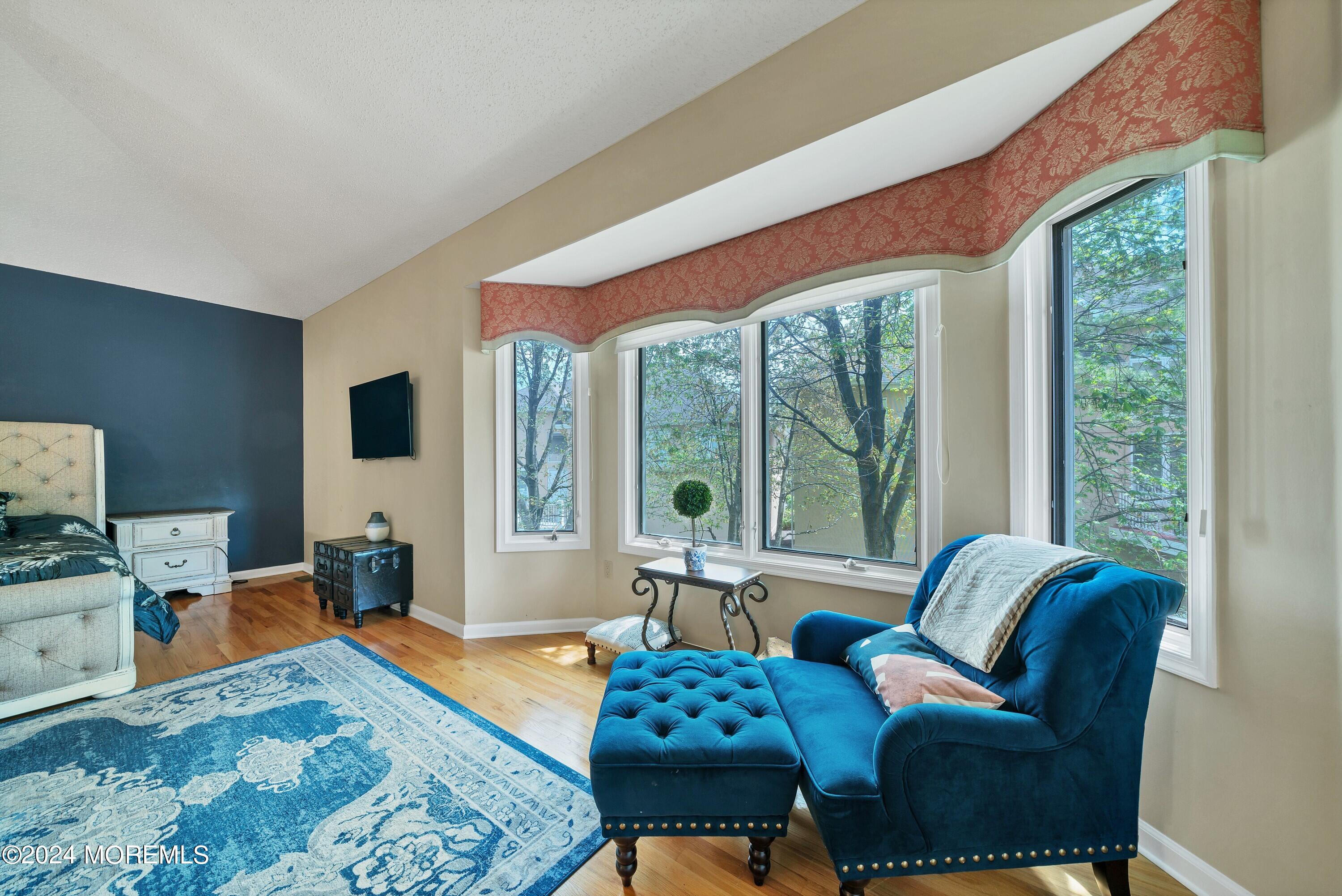 Bedroom with blue chair and ottoman beside large windows and a red patterned valance.
