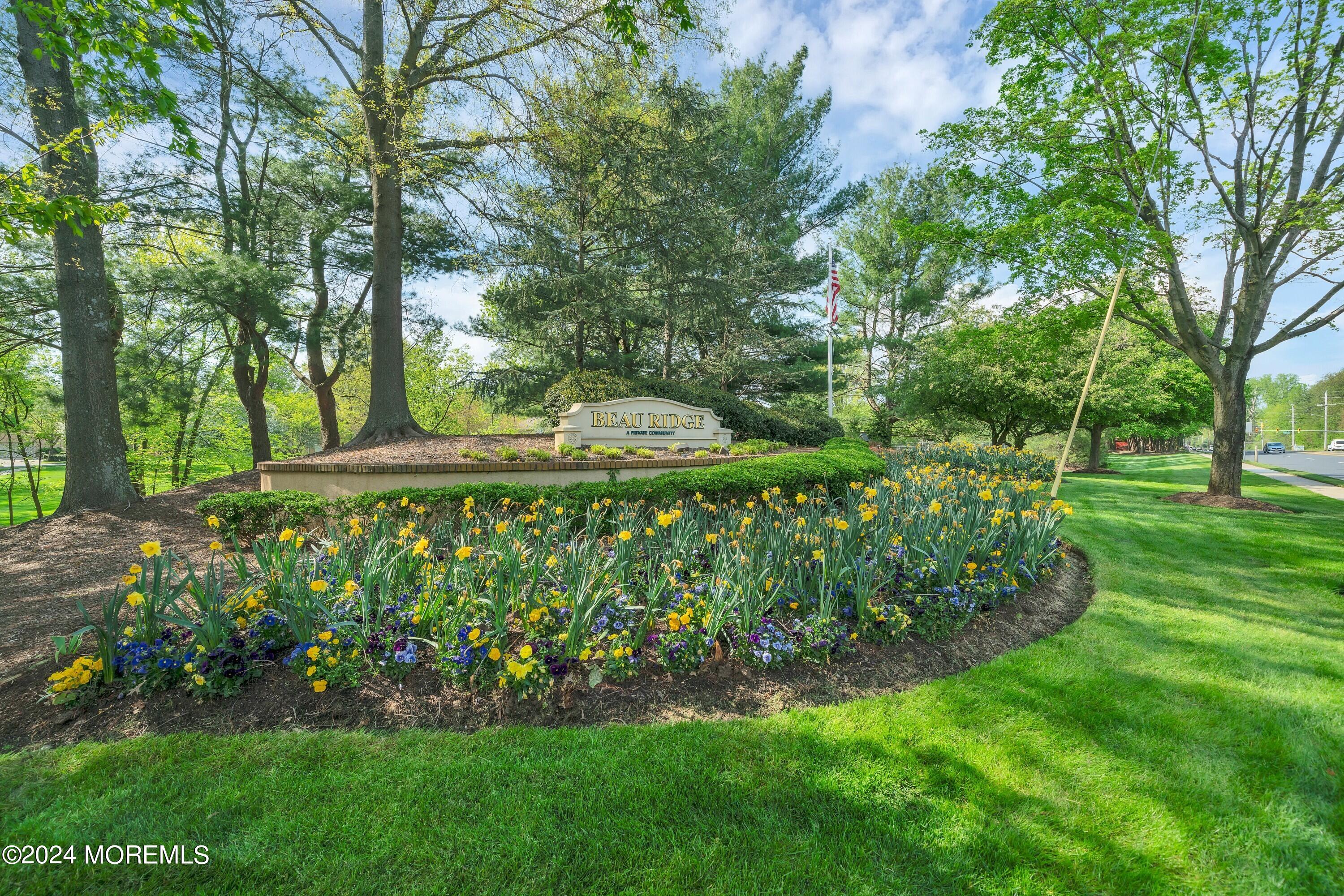 Beau Ridge community entrance sign among spring flowers and mature trees.