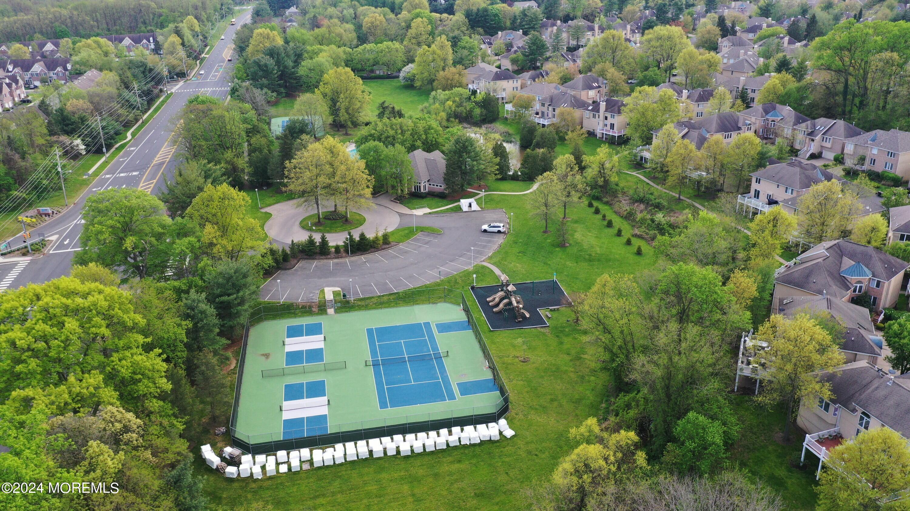 Aerial view of a residential community with tennis courts, a playground, and tree-lined grounds.