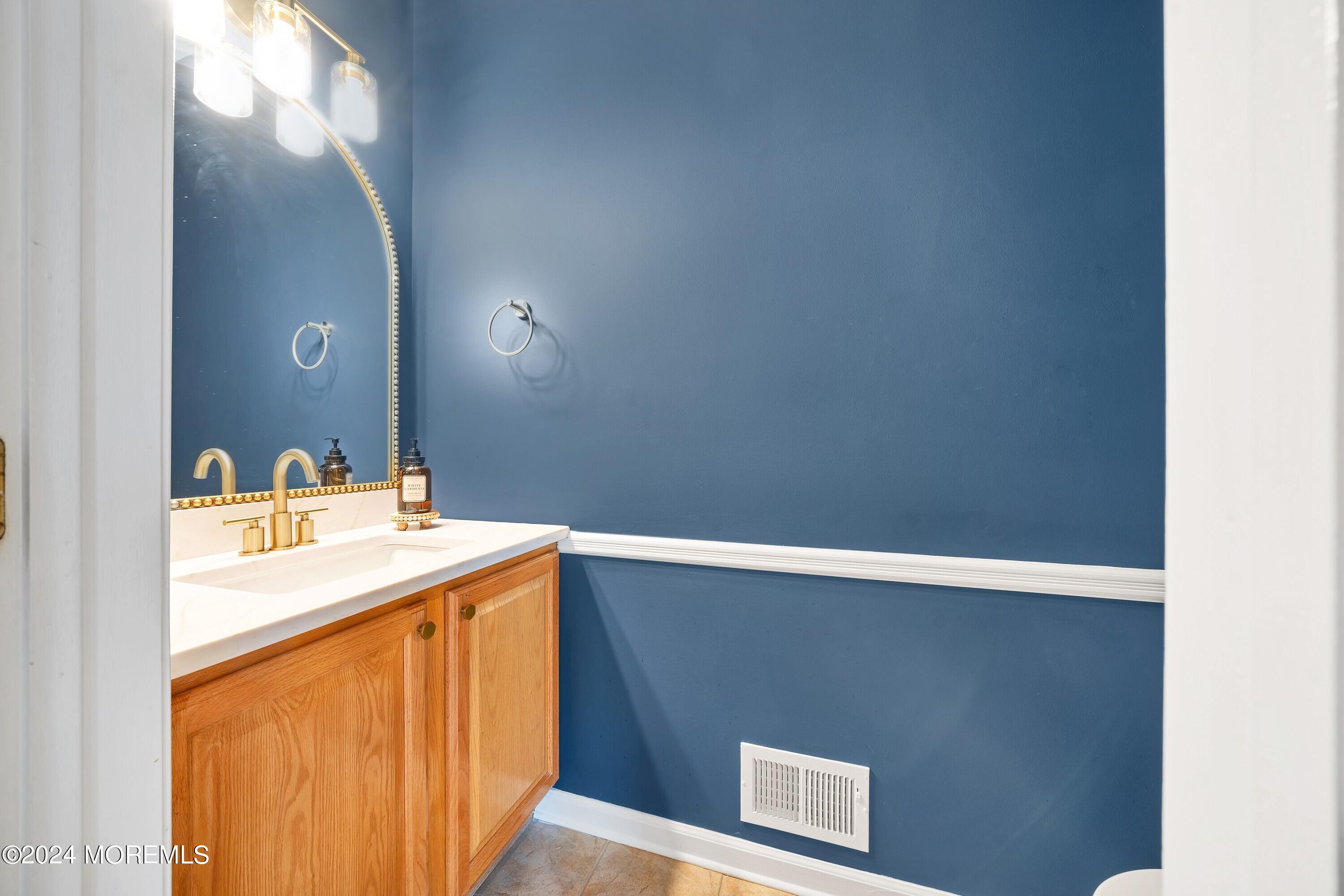 Bathroom vanity with oak cabinets, brass faucet, and a mirror against deep blue walls.