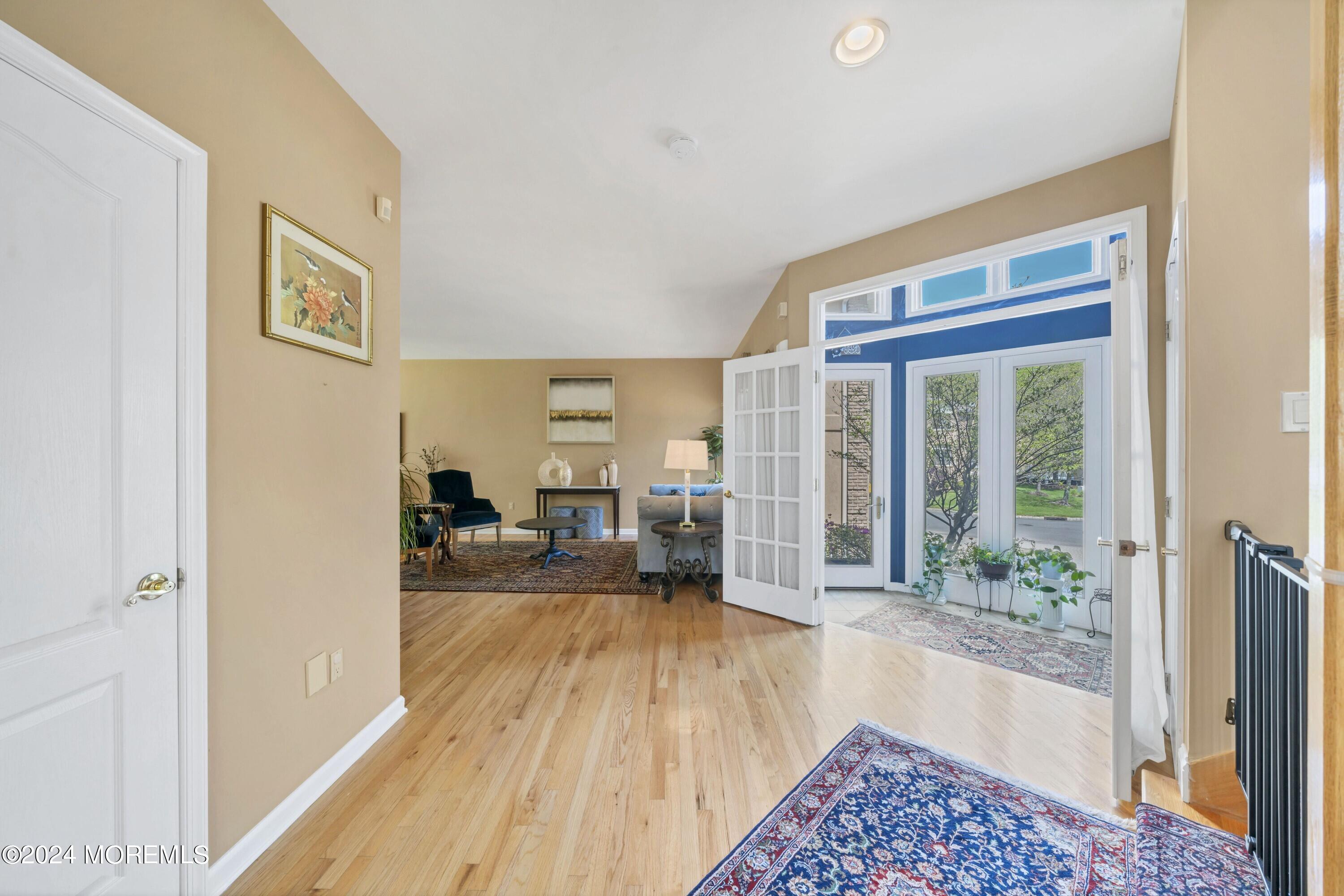 Entry hall with hardwood floors opening through French doors to a sunny, plant-filled sunroom.