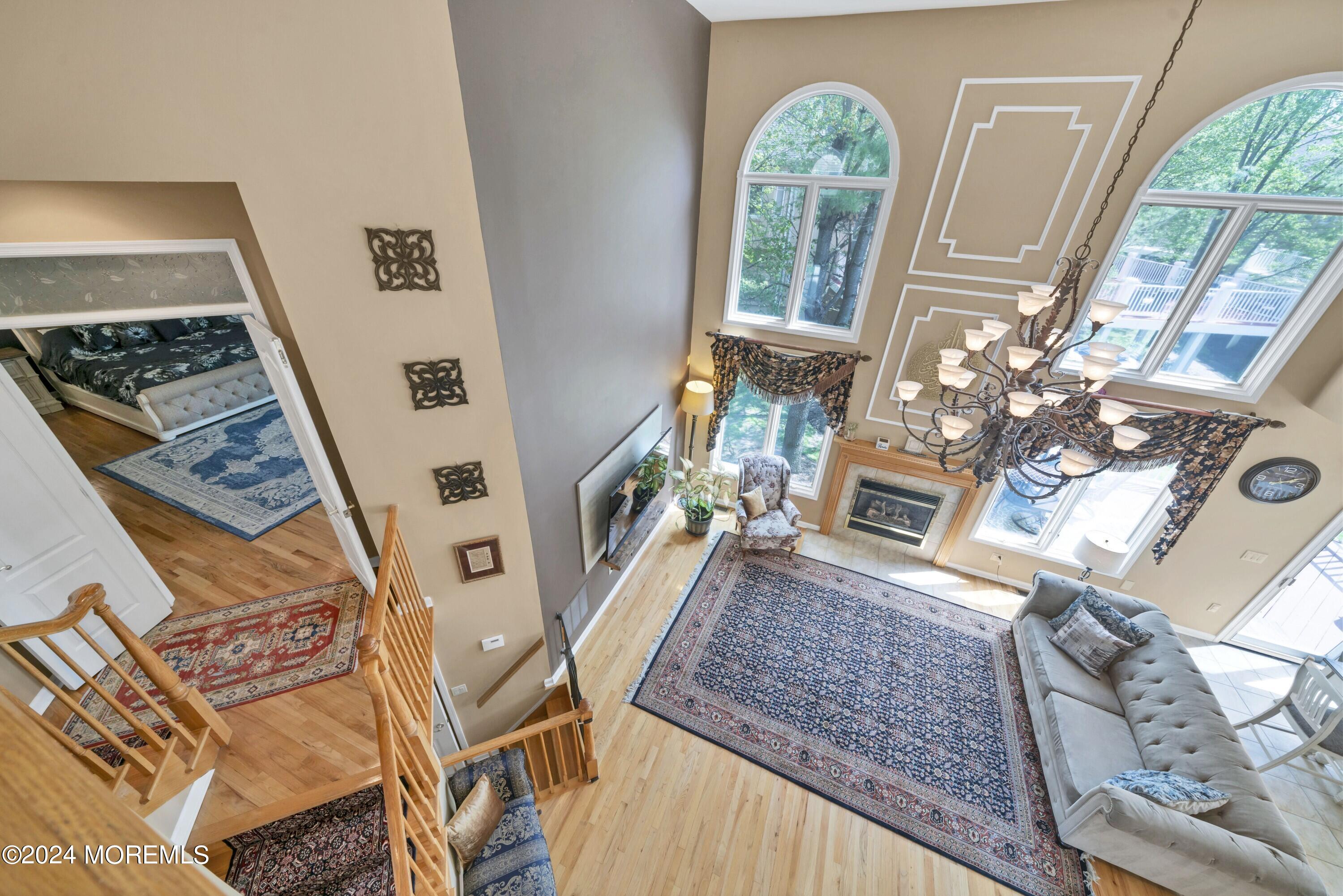 Double-height living room with arched windows, fireplace, chandelier, and overlooking staircase.