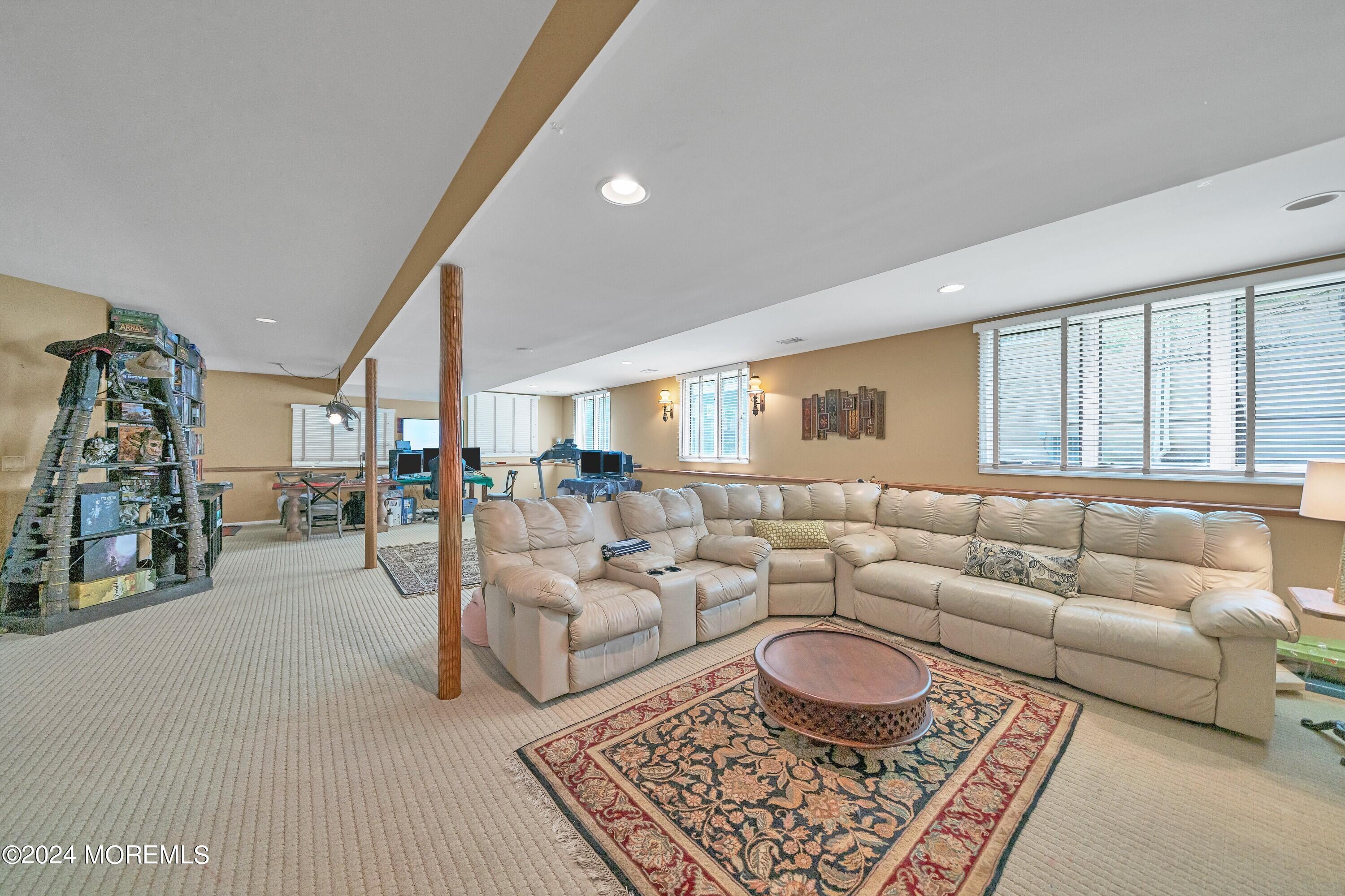 Furnished basement recreation room with a beige sectional, patterned rug, and computer workstations.