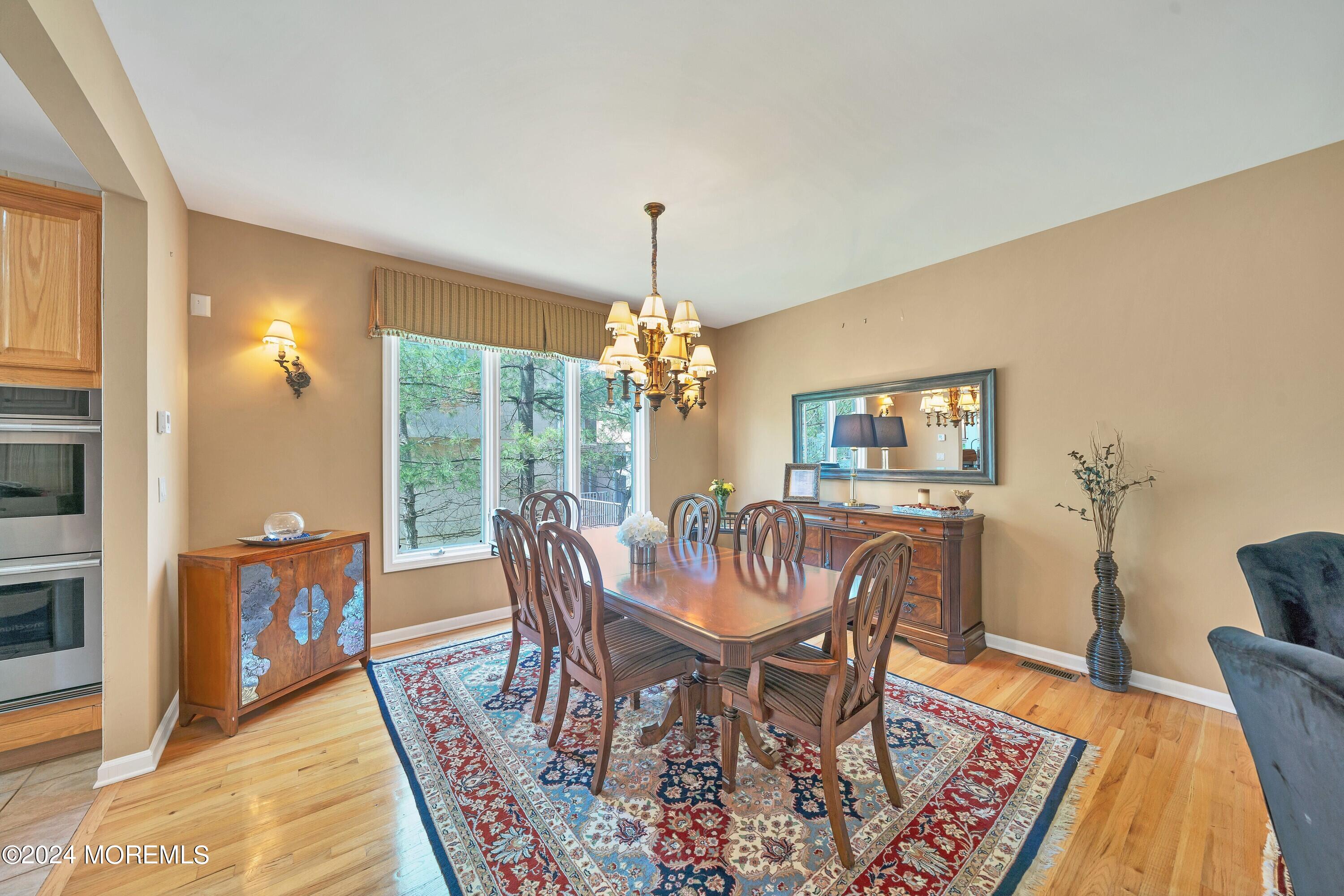 Dining room with carved wooden furniture, a chandelier, patterned rug, and large window overlooking trees.