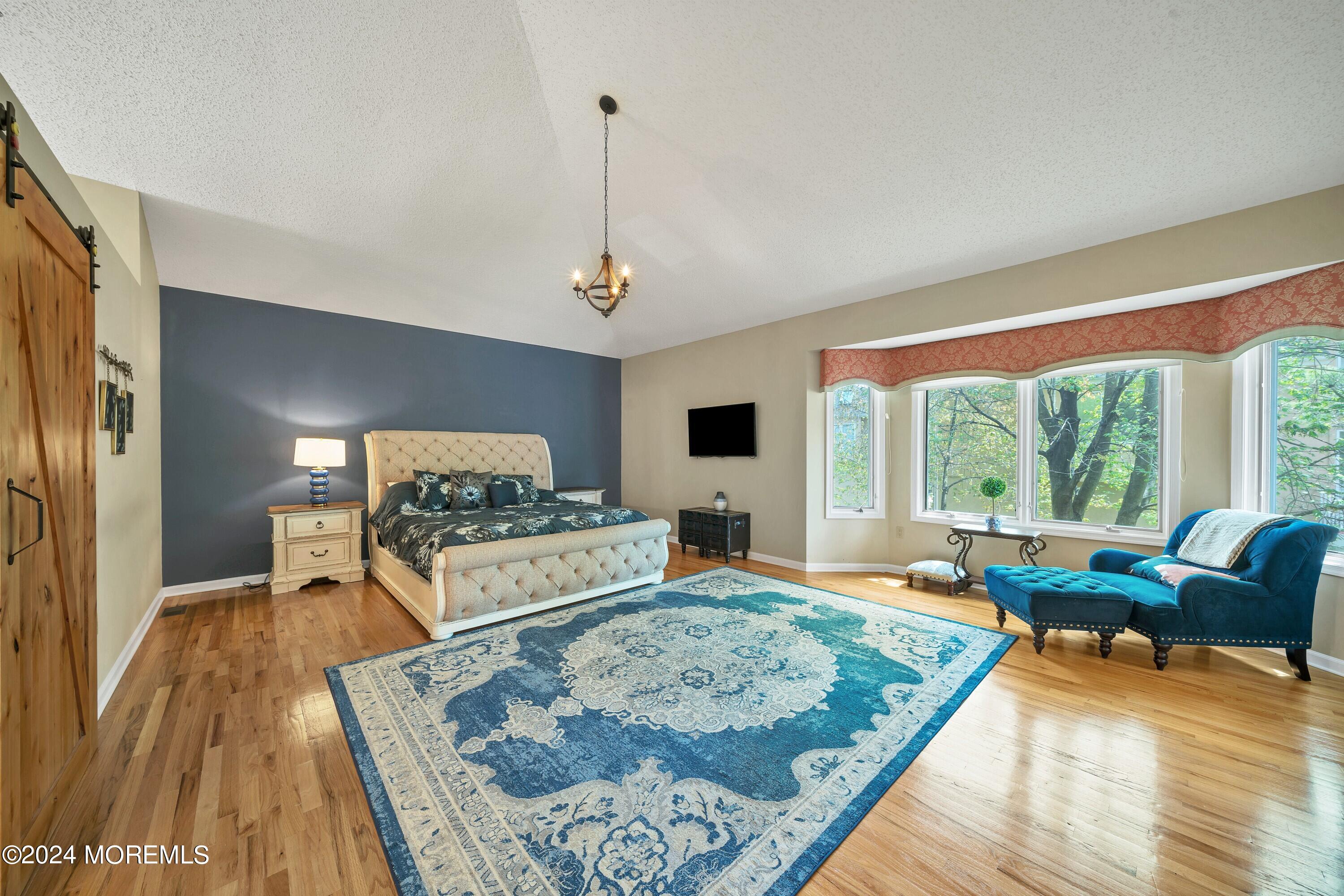 Furnished bedroom with a tufted cream bed, blue patterned rug, and bright bay window.