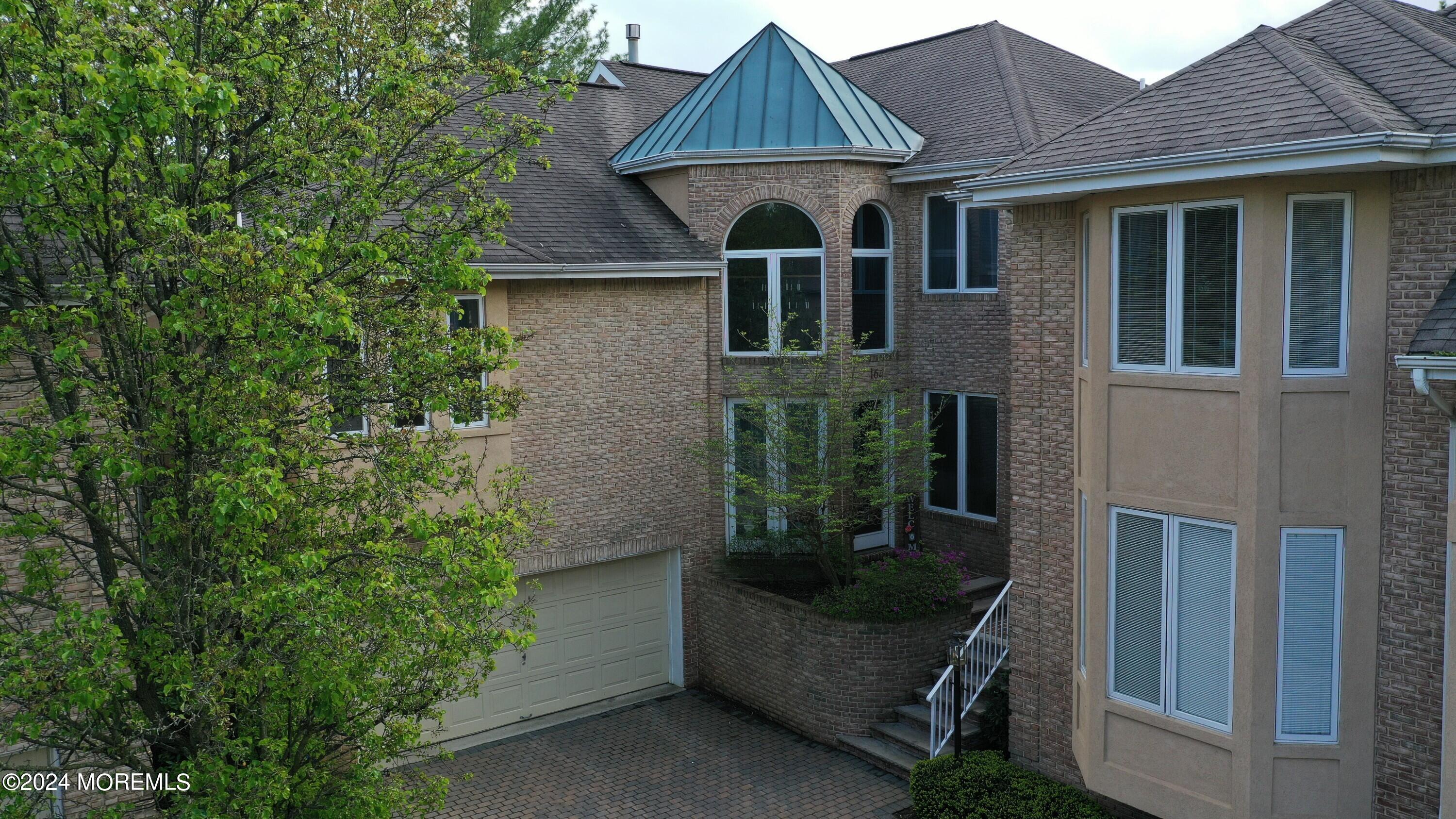 Two-story brick-and-stucco house with arched windows, blue metal roof accent, and attached garage.
