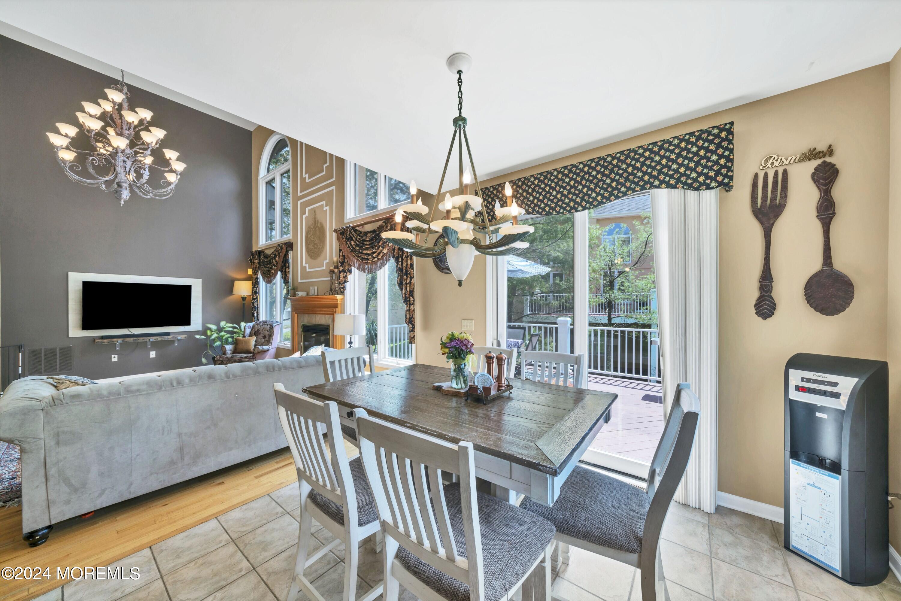 Open-plan living and dining room with two chandeliers, a fireplace, and sliding doors to a deck.