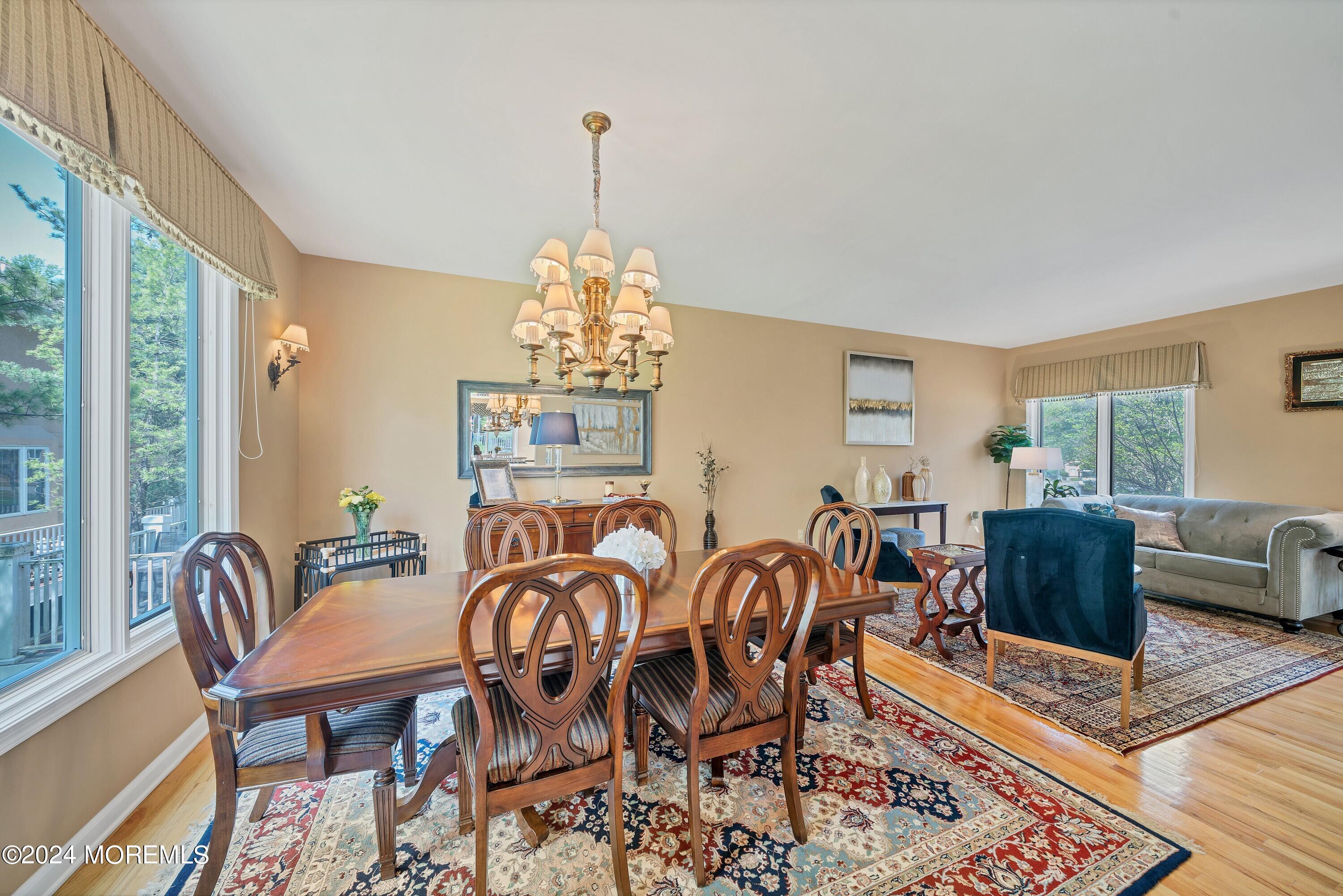 Furnished dining room with carved wood table, chandelier, large windows, and adjoining living area.