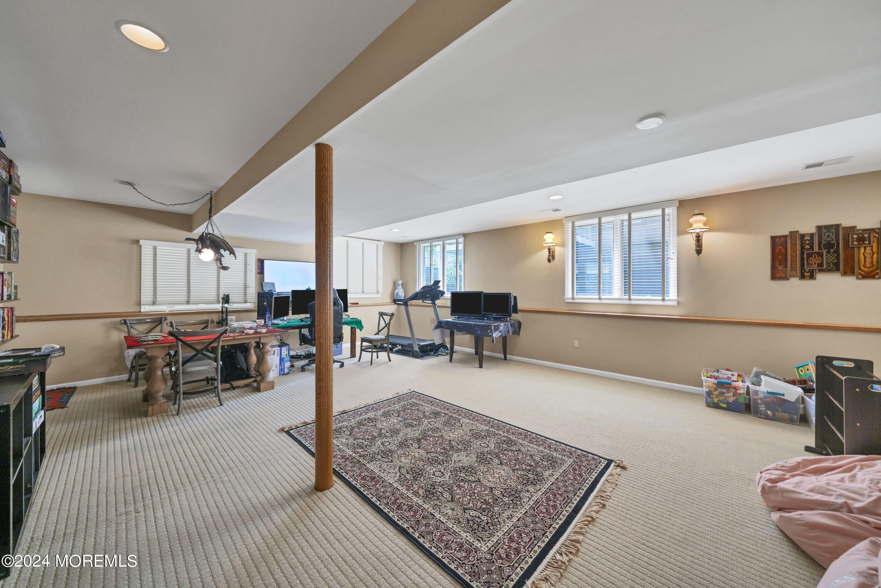 Spacious recreation room with a treadmill, computer desks, game table, and patterned rug.