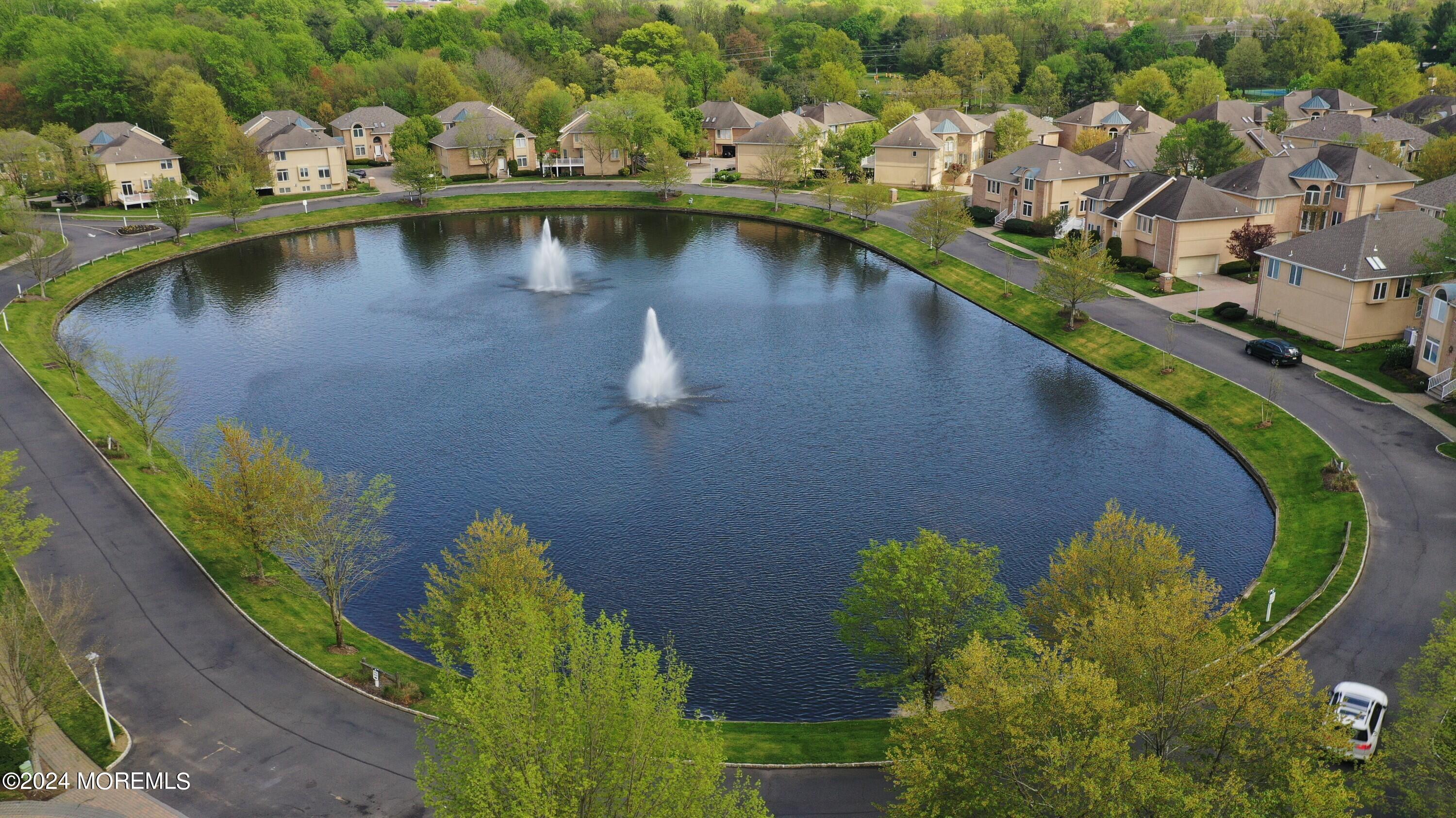 Aerial view of a residential pond with two fountains and homes lining its landscaped shore.