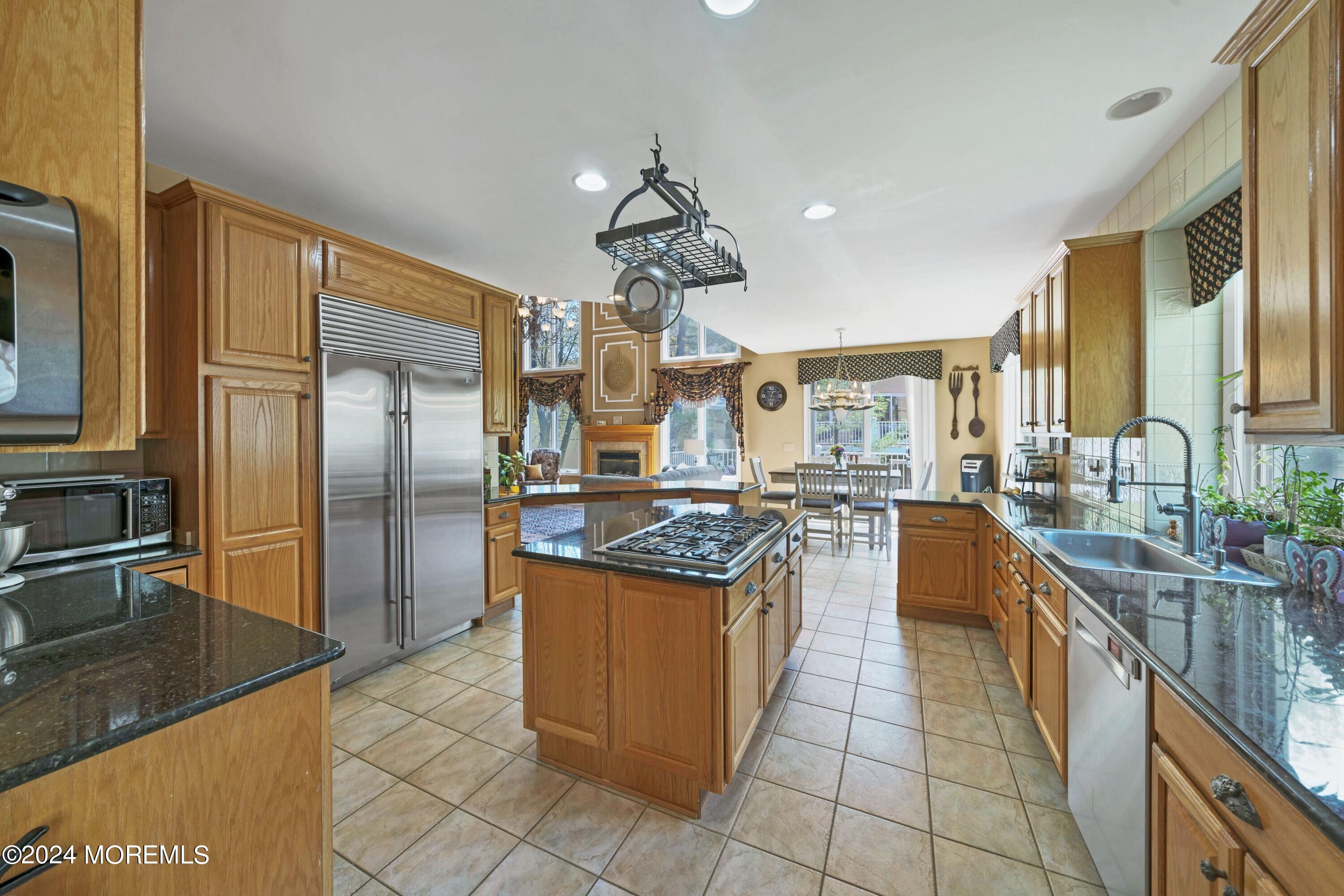 Spacious wood-cabinet kitchen with granite counters, central gas cooktop island, and stainless steel appliances.