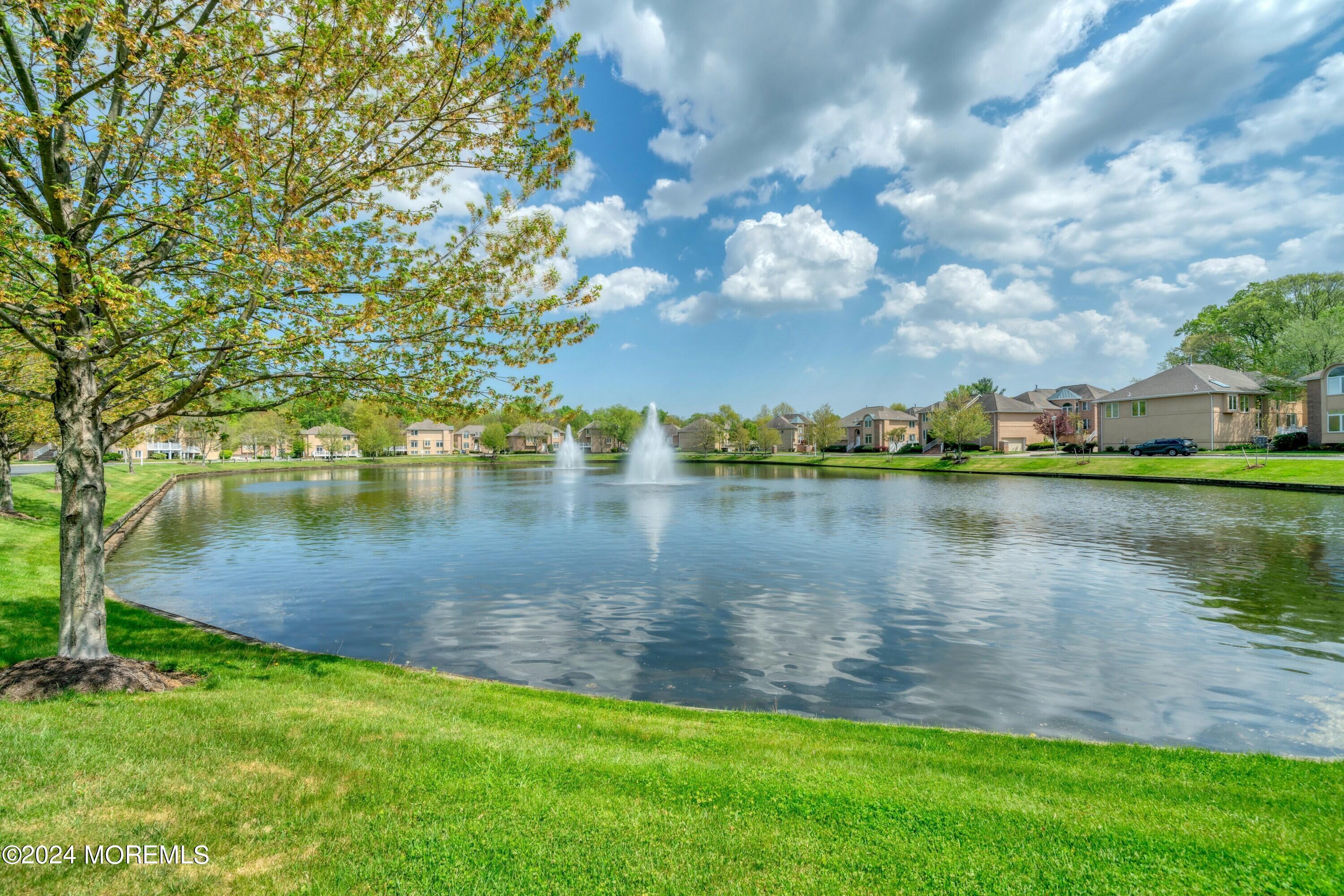 Neighborhood pond with two fountains, lawns, and homes along the far shore.