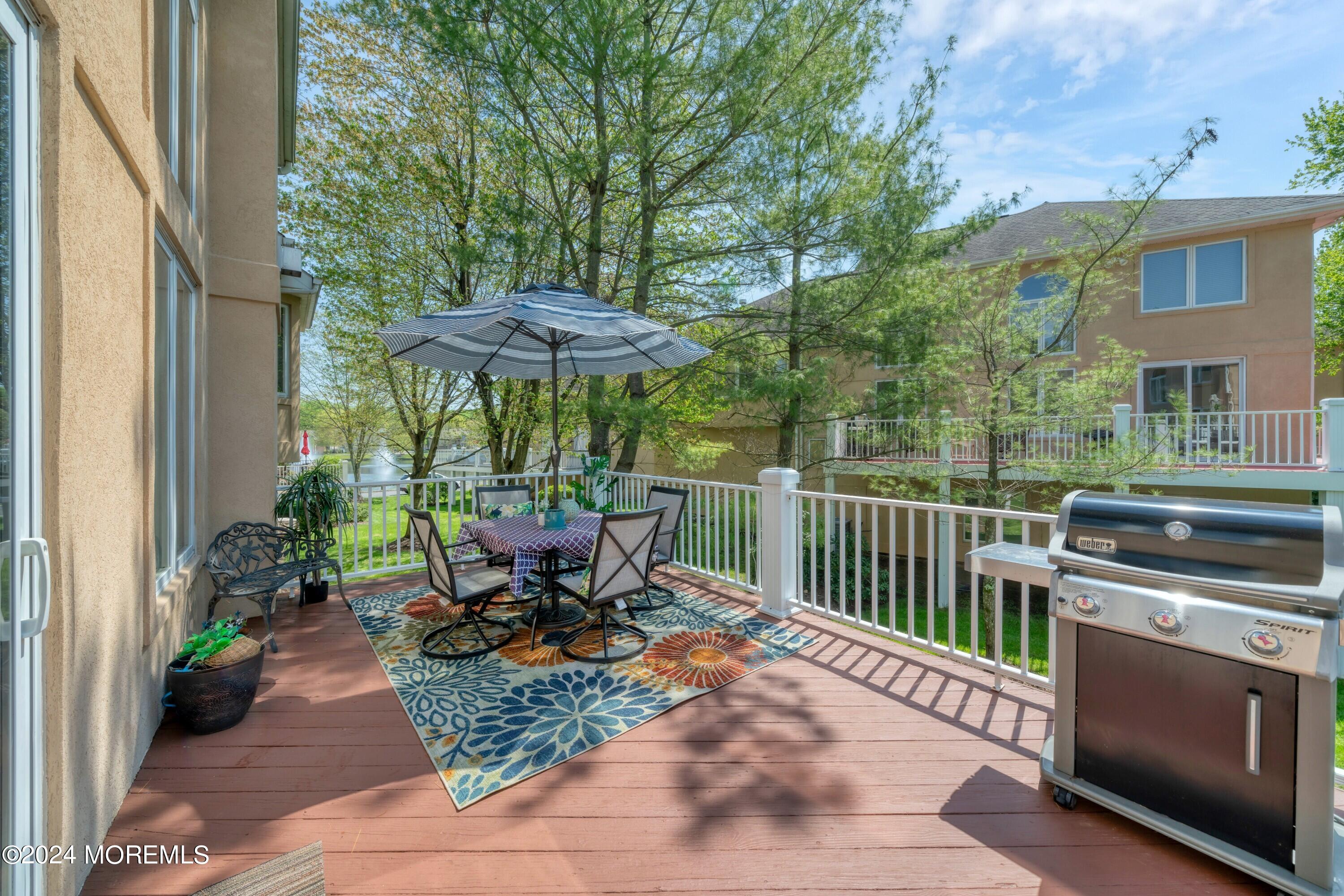 Furnished deck with umbrella-shaded dining table, patterned rug, and stainless-steel grill.