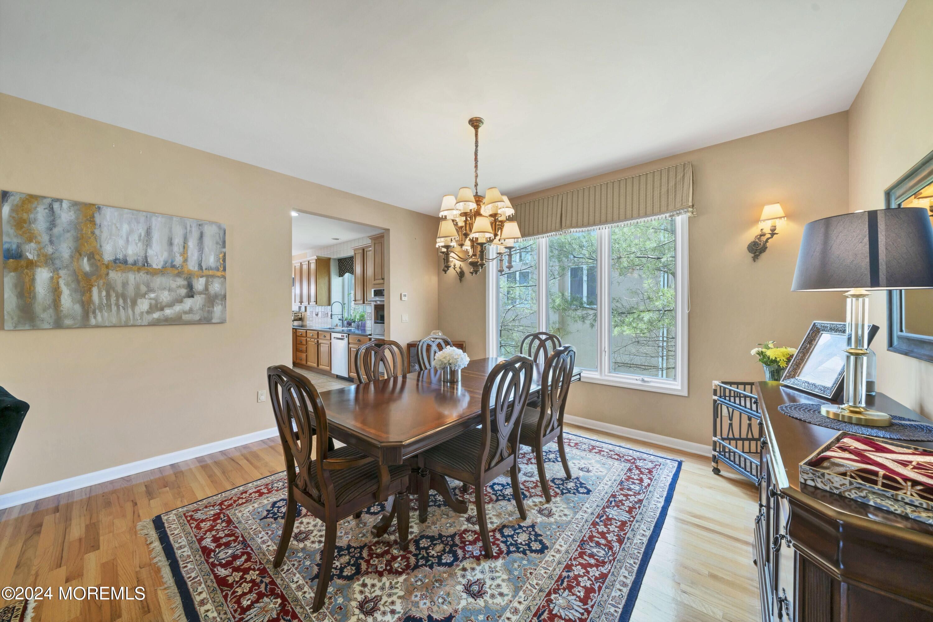 Dining room with a dark wood table, ornate chandelier, patterned rug, and large windows.