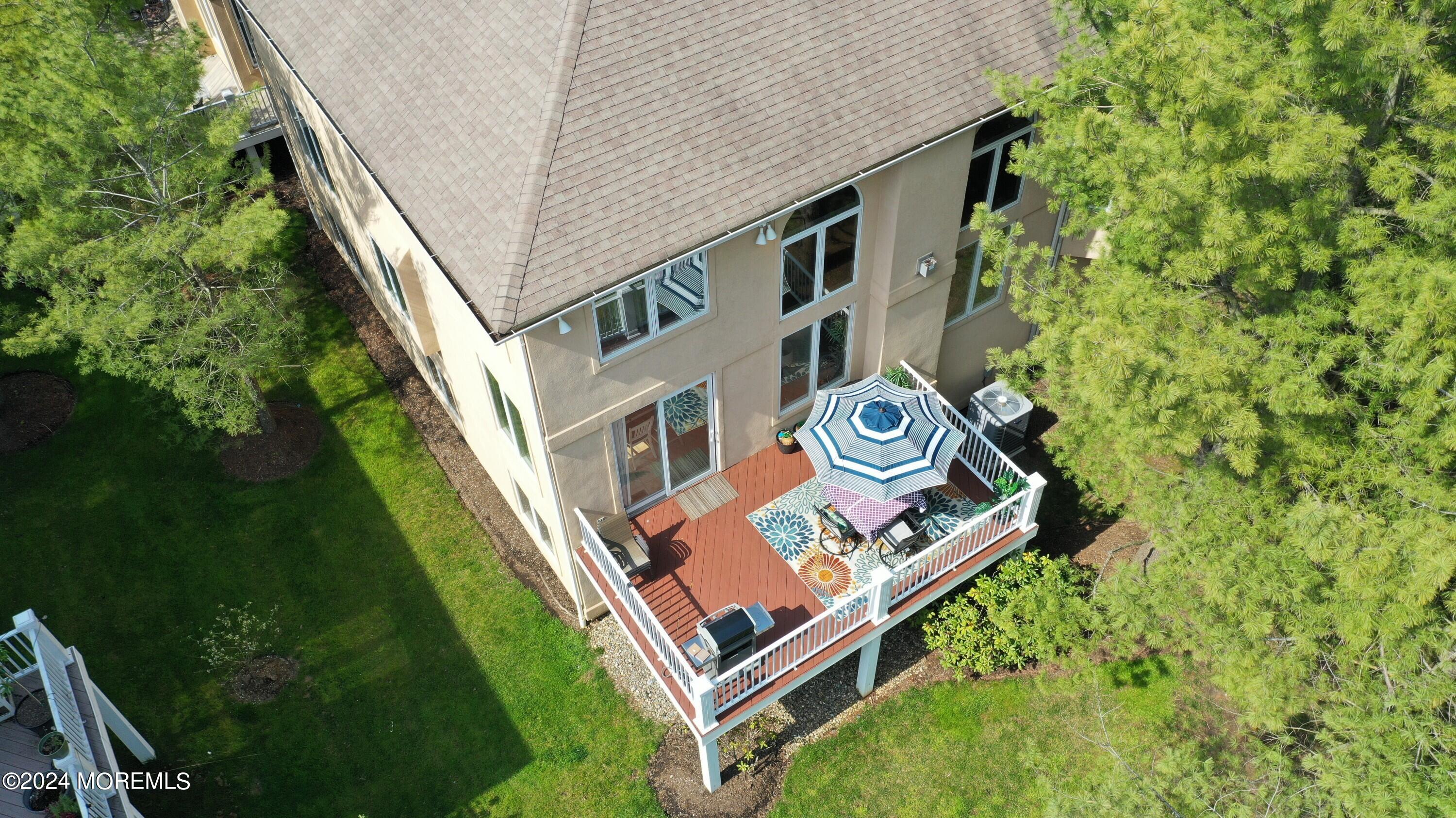 Aerial view of a two-story home and raised deck with patio furniture and a blue-and-white umbrella.
