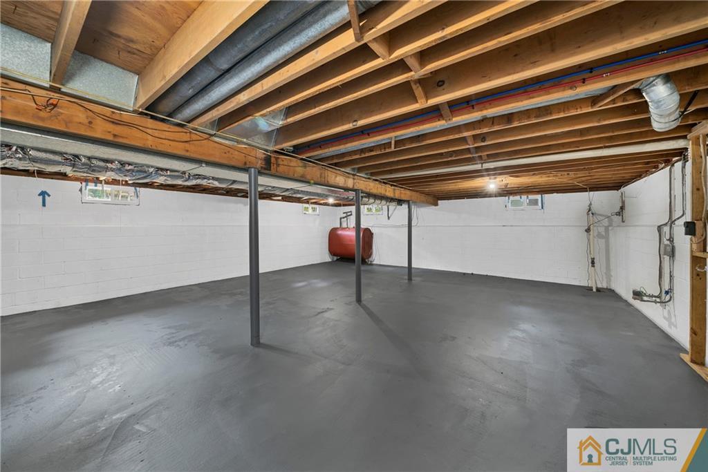 Unfinished basement with a concrete floor, exposed ceiling joists, support posts, and a red tank.