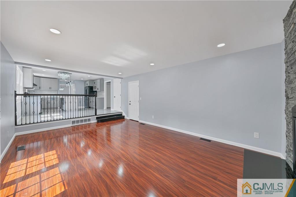 Empty living room with glossy hardwood floors, open to a raised kitchen with white cabinets and a black railing.