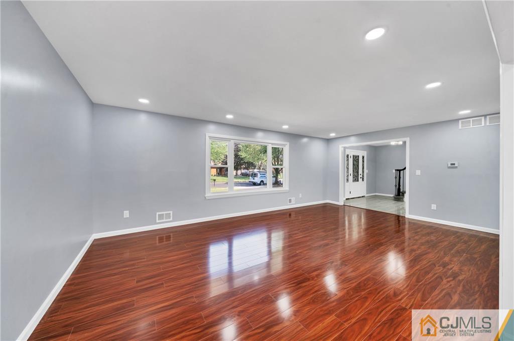 Empty living room with glossy reddish-brown flooring, gray walls, and a wide front window.