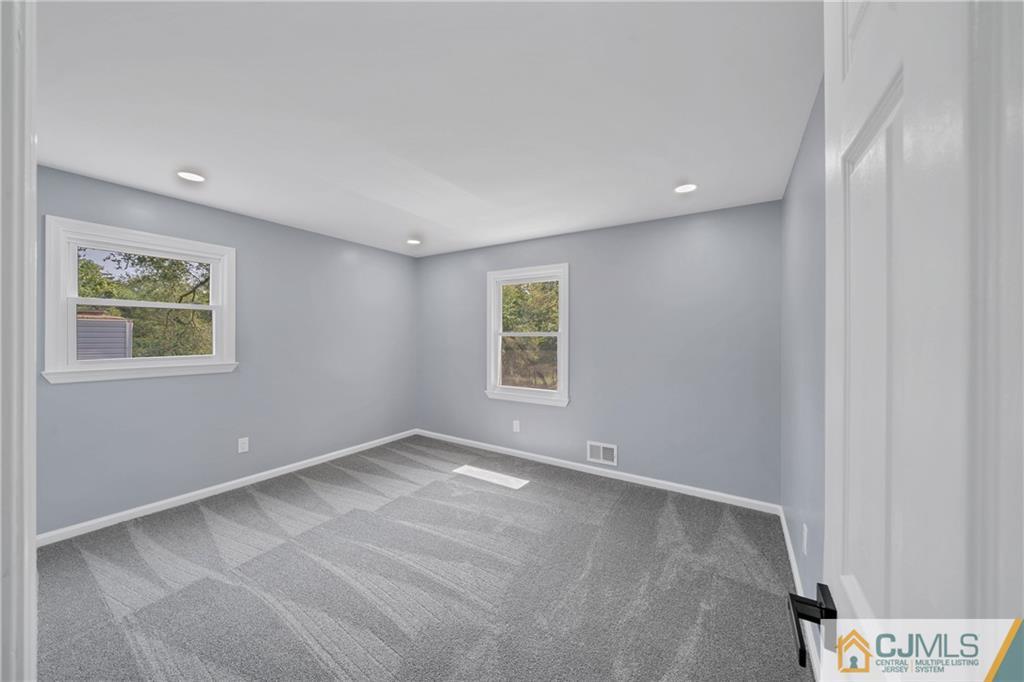 Empty bedroom with gray walls, patterned carpet, and two white-trimmed windows.