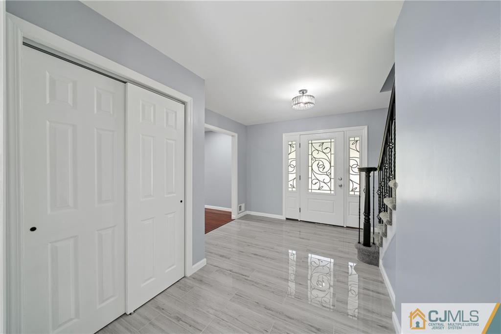 Entry foyer with glossy gray flooring, a decorative glass front door, and a staircase.