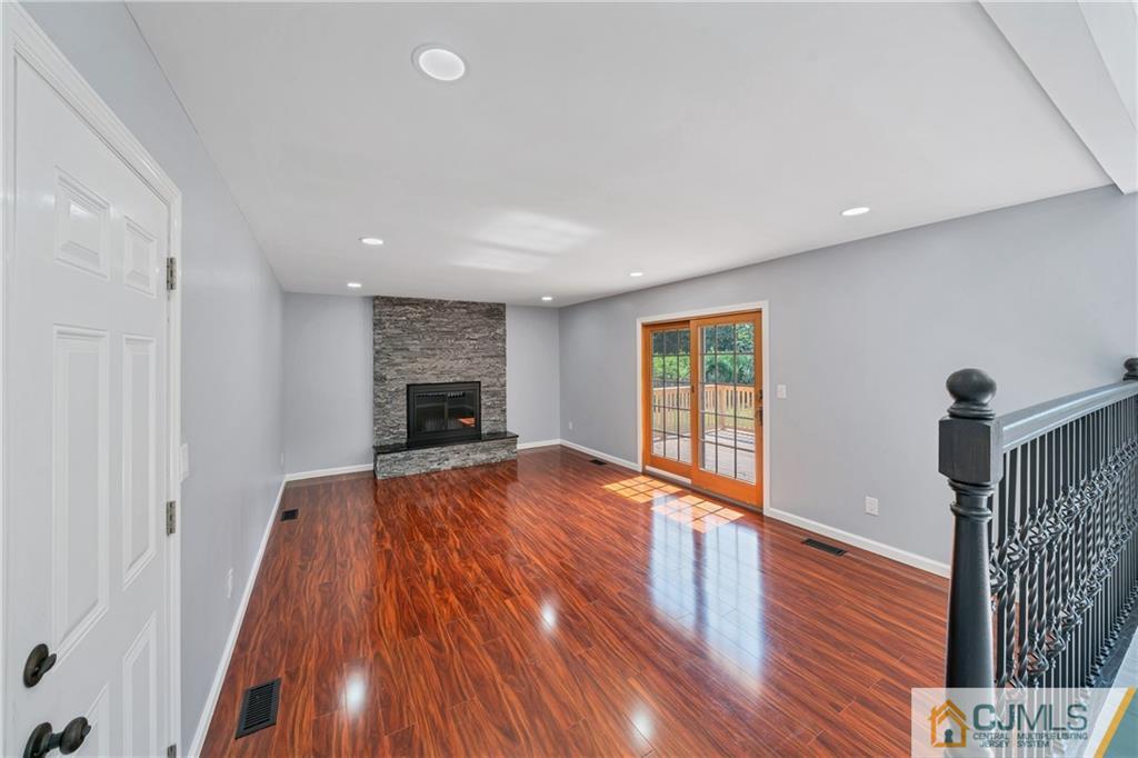 Empty living room with glossy hardwood floors, a stone fireplace, and sliding glass doors to a deck.