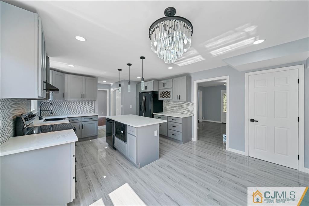 Modern kitchen with gray cabinets, a large island, patterned backsplash, and crystal chandelier.
