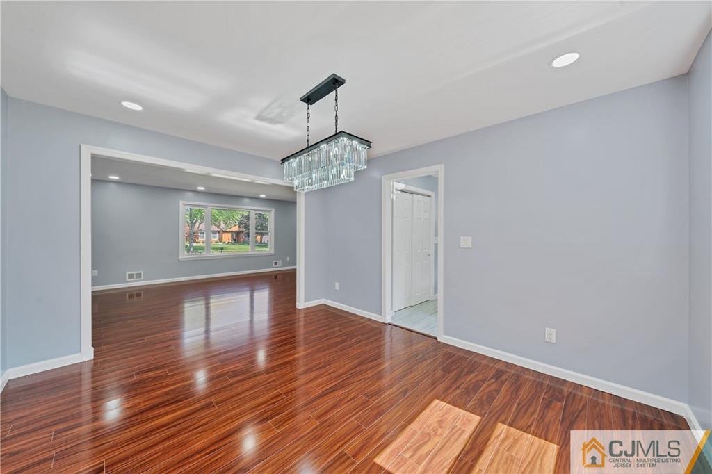 Empty dining area with glossy hardwood floors and a crystal chandelier, opening into a room with a large window.
