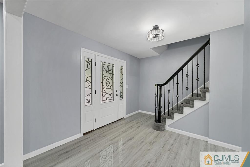 Entry foyer with decorative glass front door, gray tile flooring, and carpeted staircase with black railing.