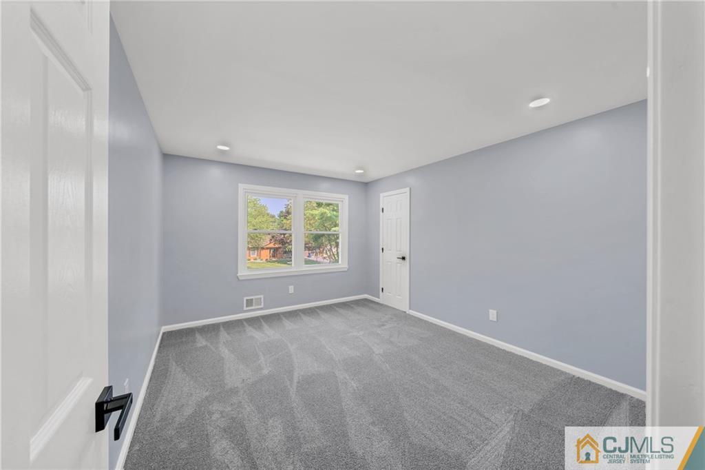Empty bedroom with gray carpet, light blue-gray walls, and a window overlooking trees.
