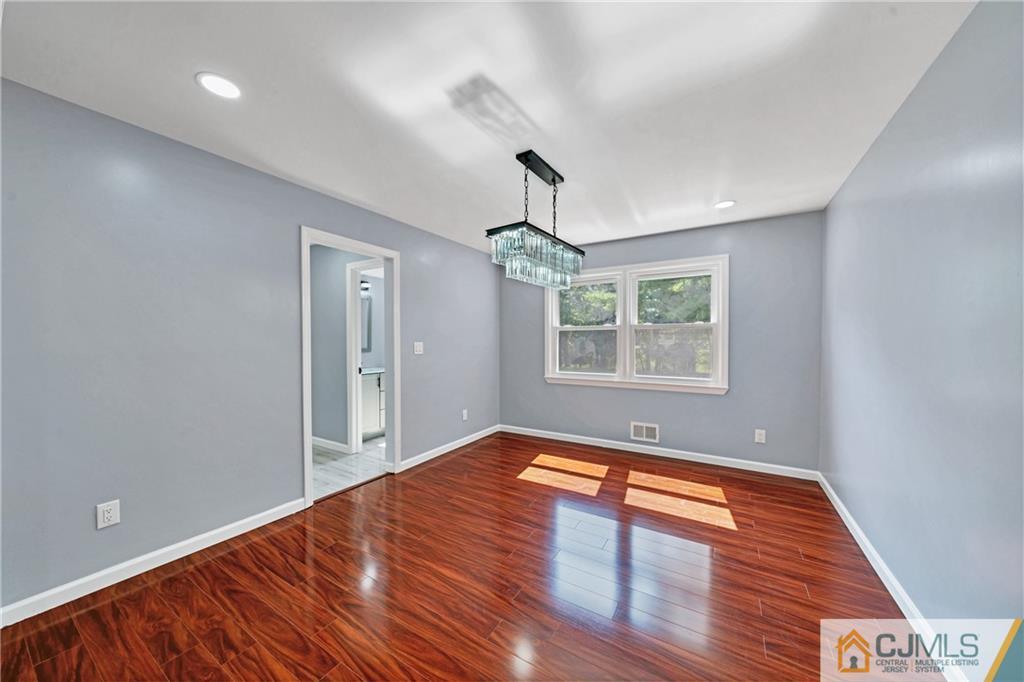 Unfurnished dining room with glossy wood floors, gray walls, and a rectangular chandelier.