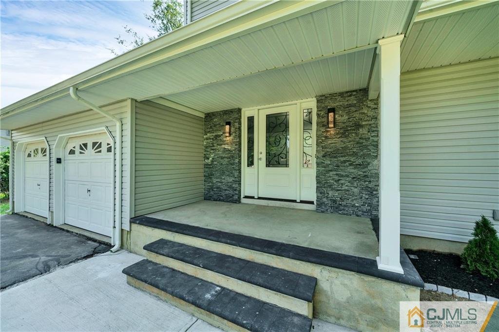 House entrance with a covered porch, stone facade, decorative glass door, and two garage doors.
