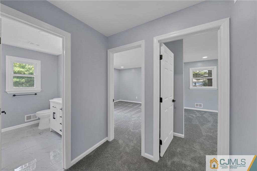 Vacant hallway with gray carpeting, opening to two rooms and a tiled bathroom.
