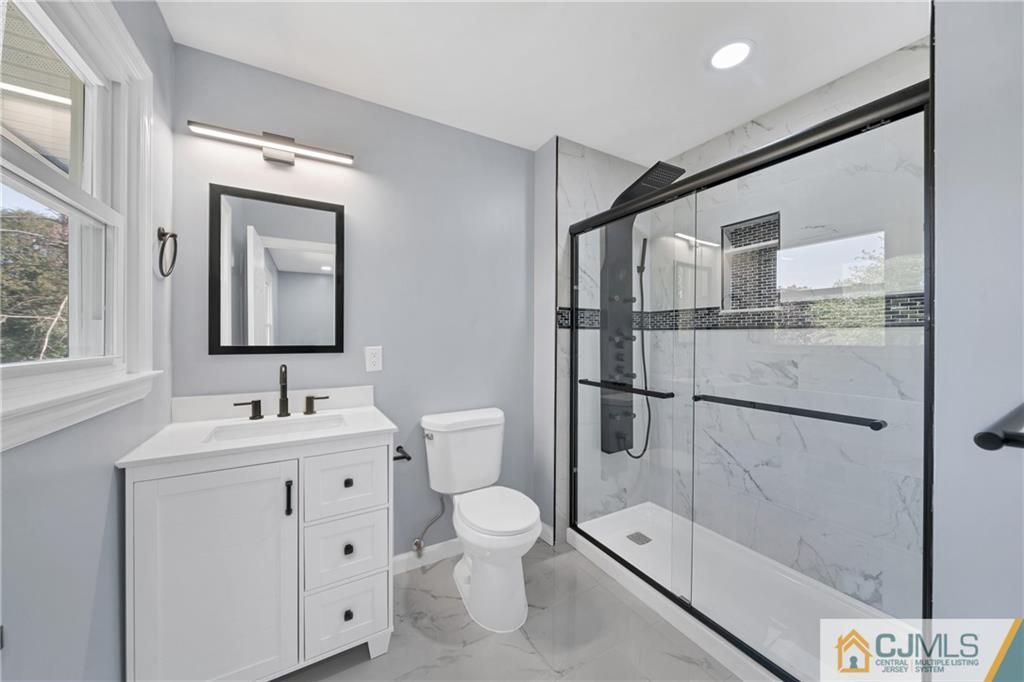 Renovated bathroom with a white vanity and a glass walk-in shower with marble-look tile.
