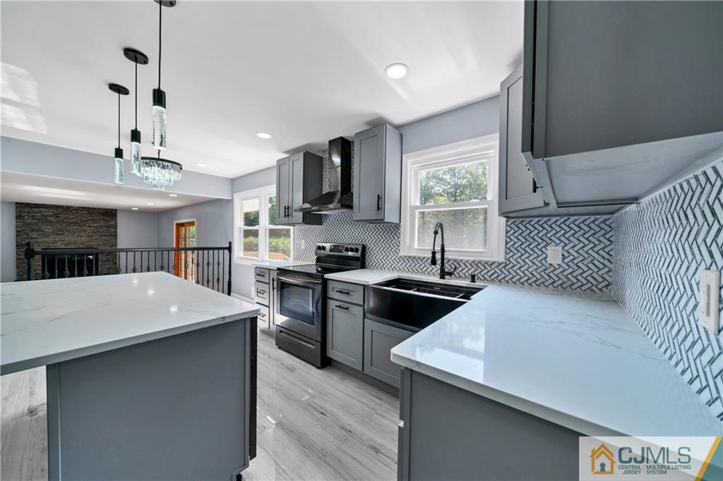 Renovated kitchen with a large white island, gray cabinets, stainless steel range, and geometric tile backsplash.